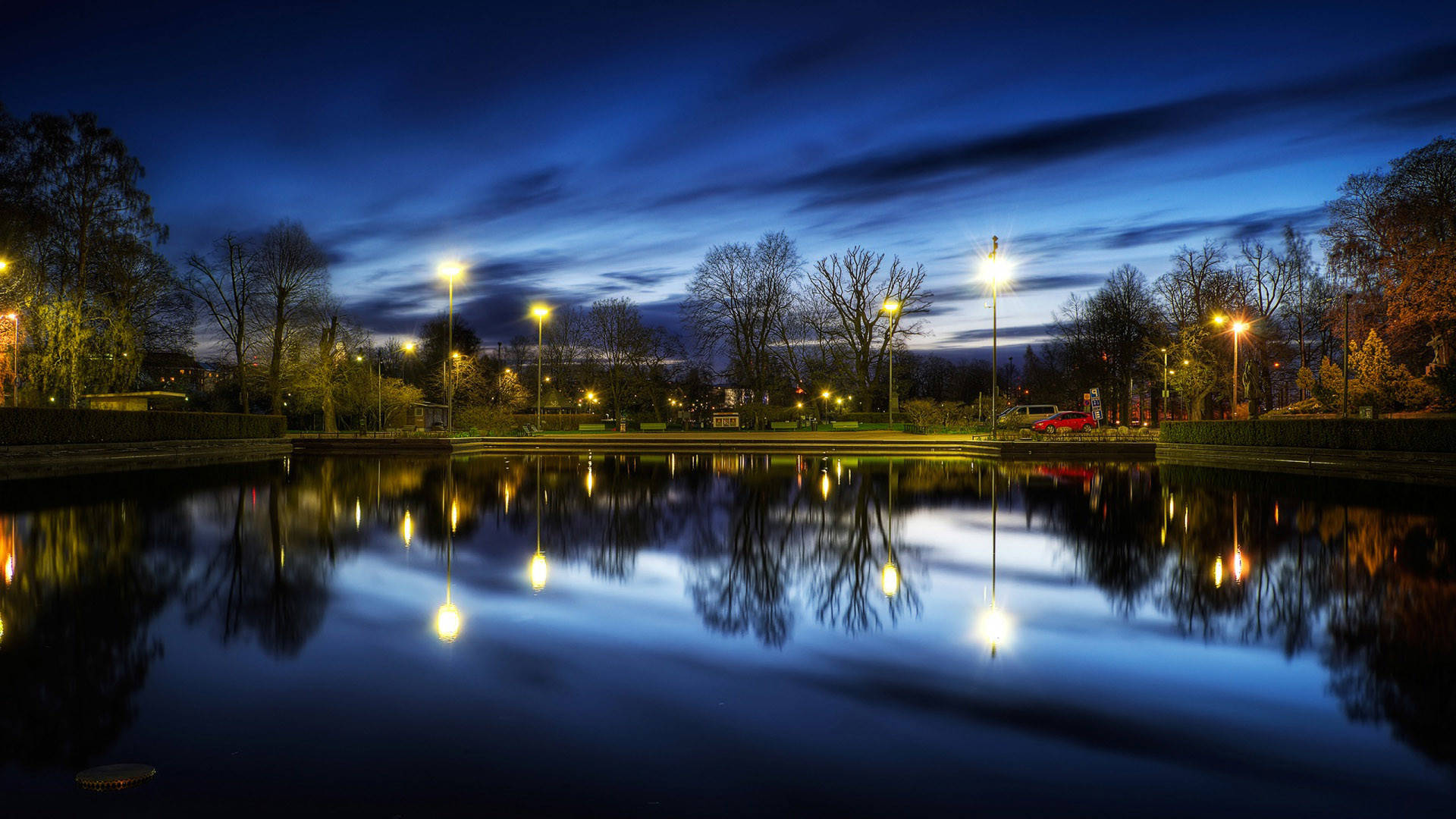Beautiful Night 桌布 壁紙 — 一個寧靜的黃昏公園池塘，在深藍色的天空下映照著發光的街燈和光禿的樹木。
