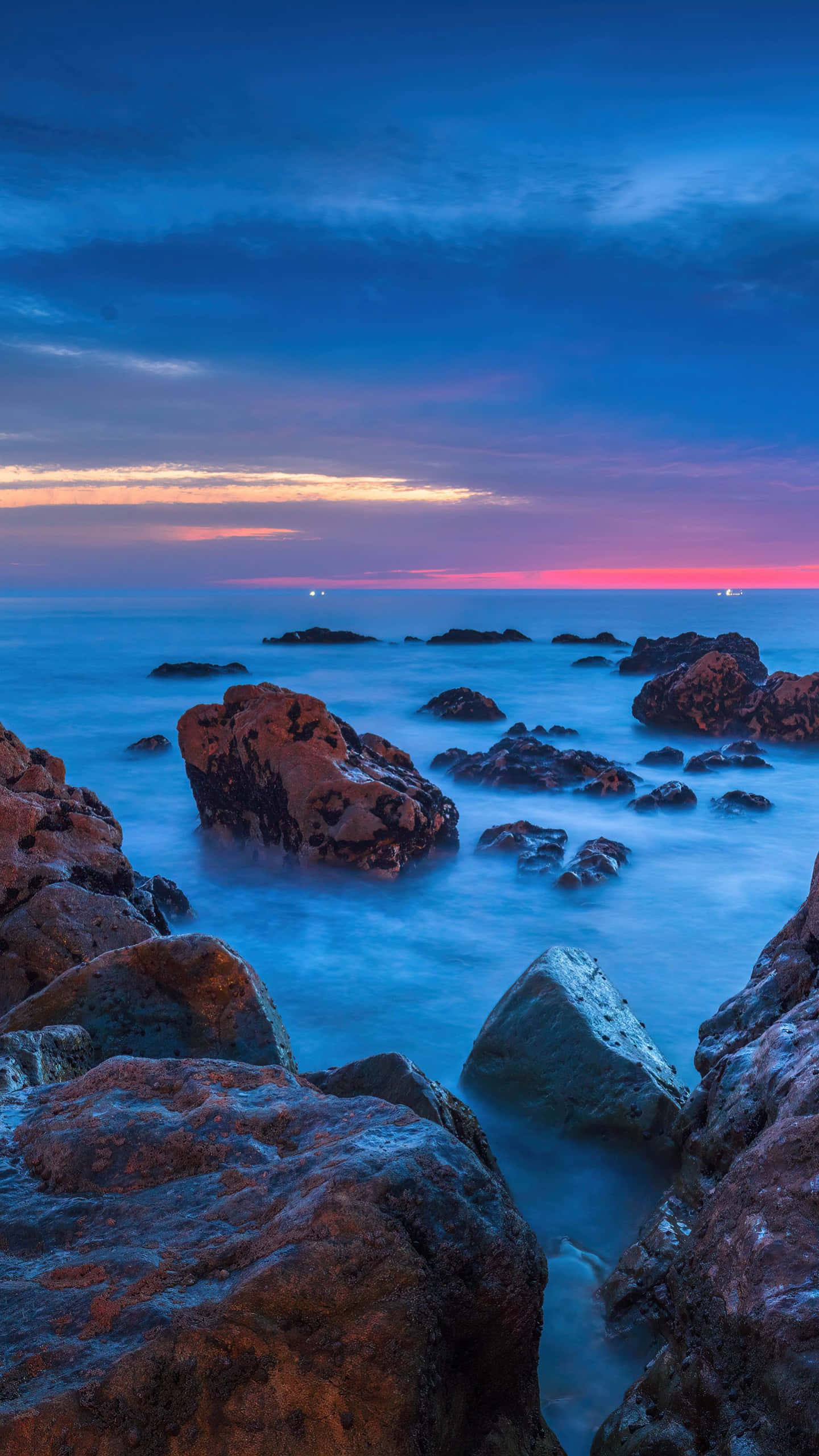 Beach Photography 桌布 壁紙 — 一個寧靜的黃昏海景，光滑的藍色水流繞過崎嶇的岩石，天空呈現深藍與柔和粉紅的漸變色。