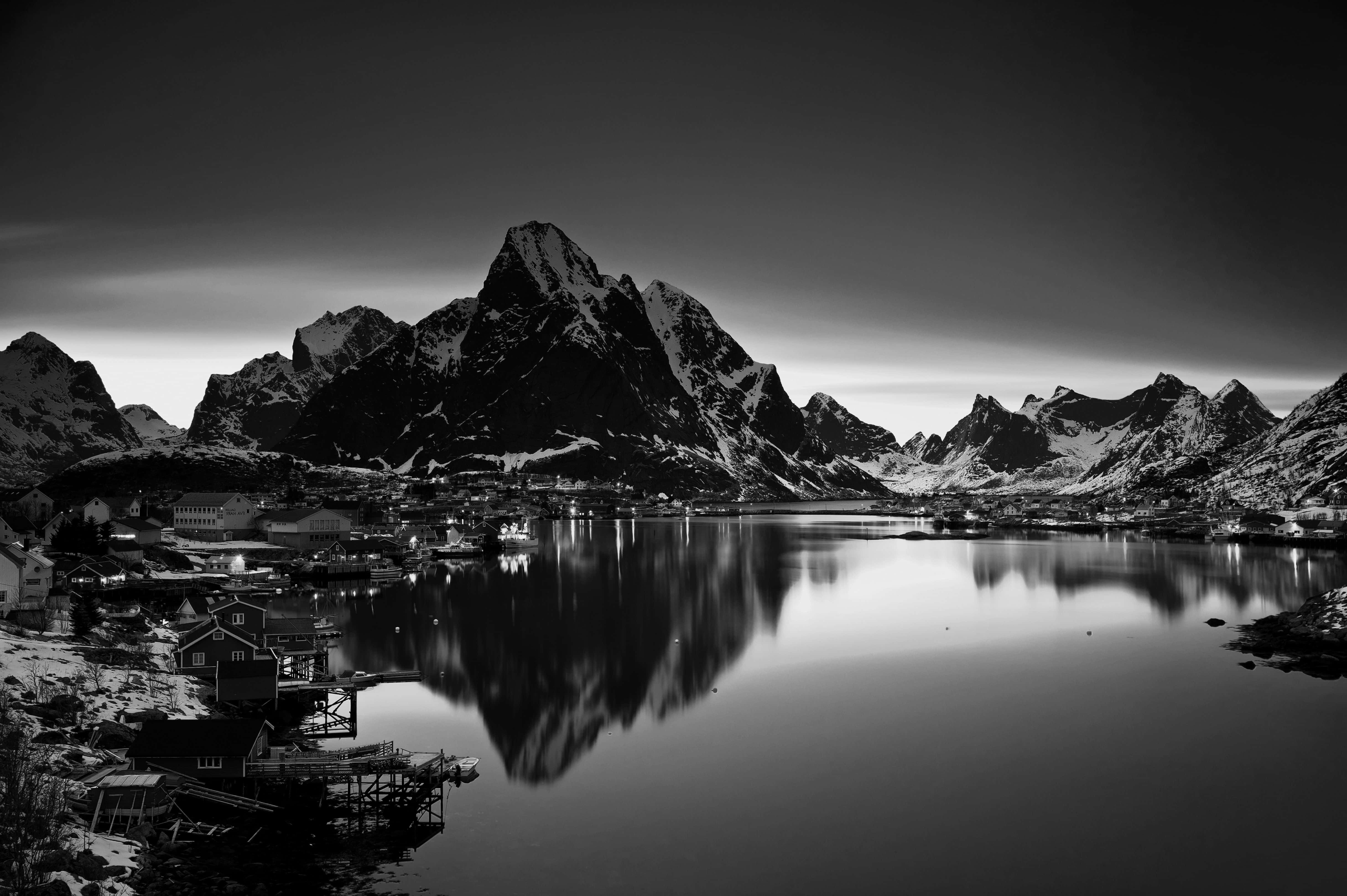 Monochrome 桌布 壁紙 — 一個寧靜的黑白風景，白雪覆蓋的山脈倒映在平靜的水面上，山腳下有一個小村莊。