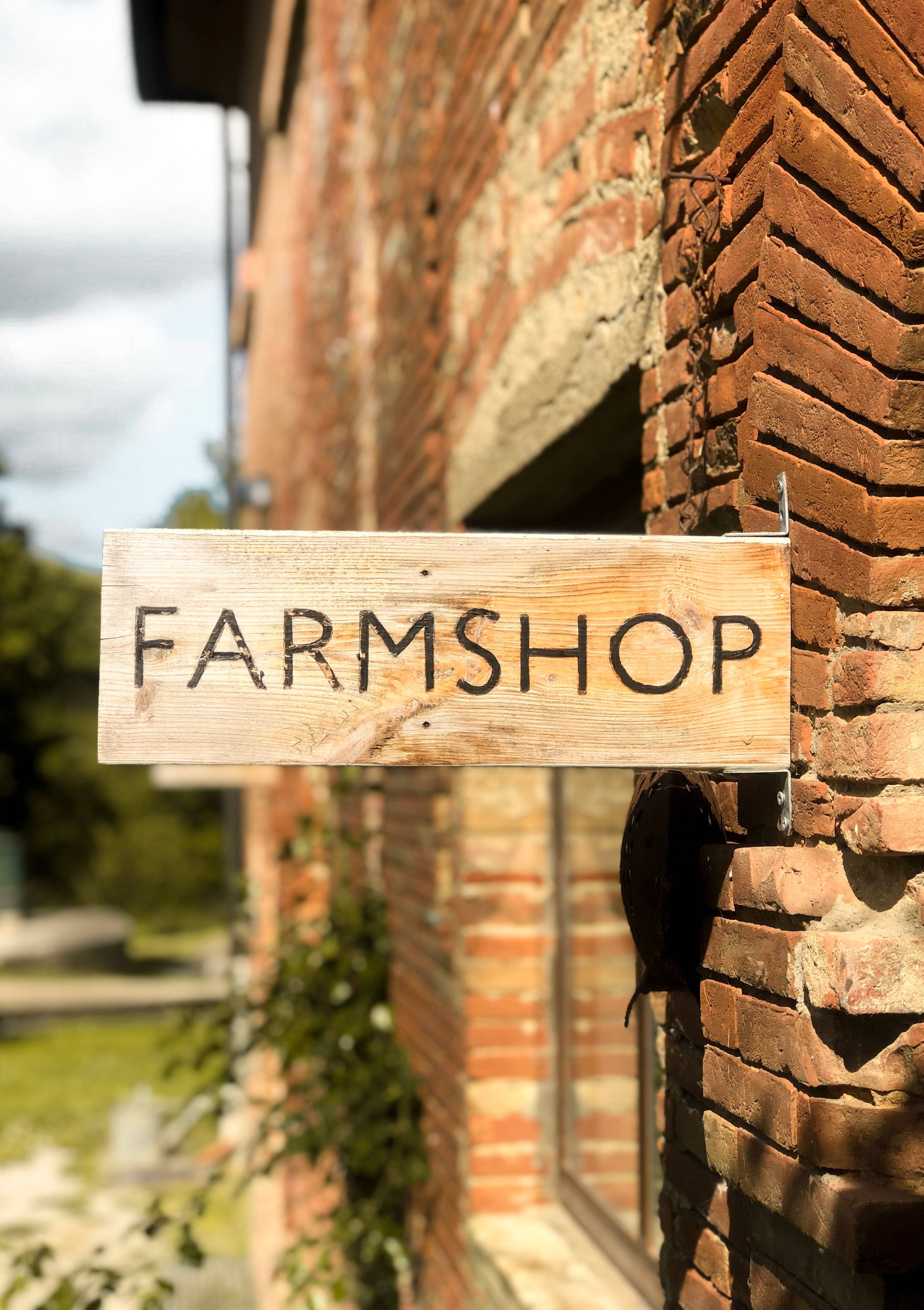 字型 桌布 壁紙 — 一個寫有 FARMSHOP 的質樸木牌掛在風化的磚牆上，在明亮的日光下。