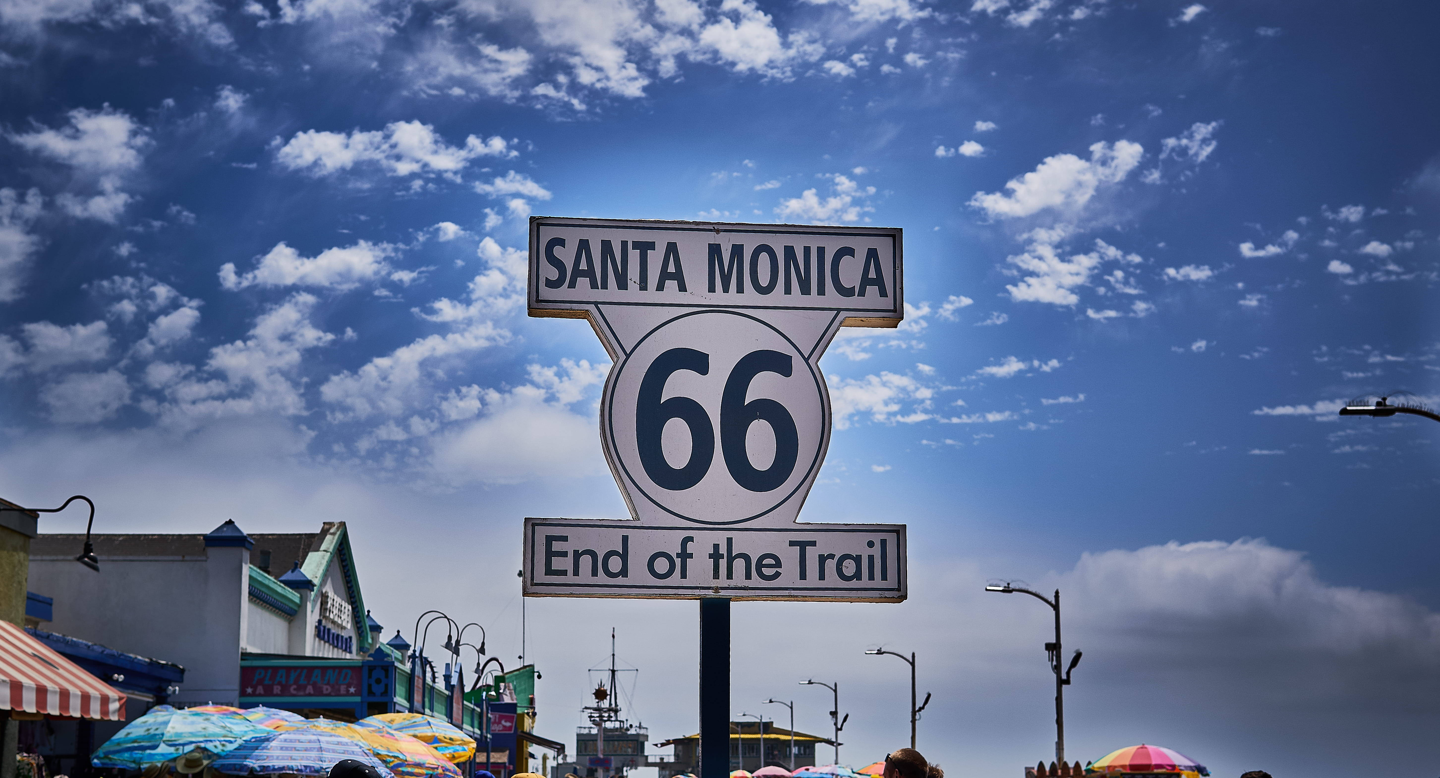 Monica 桌布 壁紙 — 一個寫有「Santa Monica End of the Trail」的復古66號公路標誌，矗立在藍天白雲下。