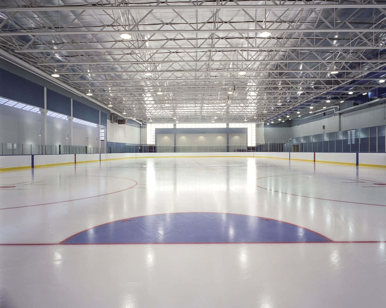 Ice Rink 桌布 壁紙 — 一個寬敞空曠的室內溜冰場，擁有拋光冰面及在明亮燈光下外露的金屬桁架天花板。