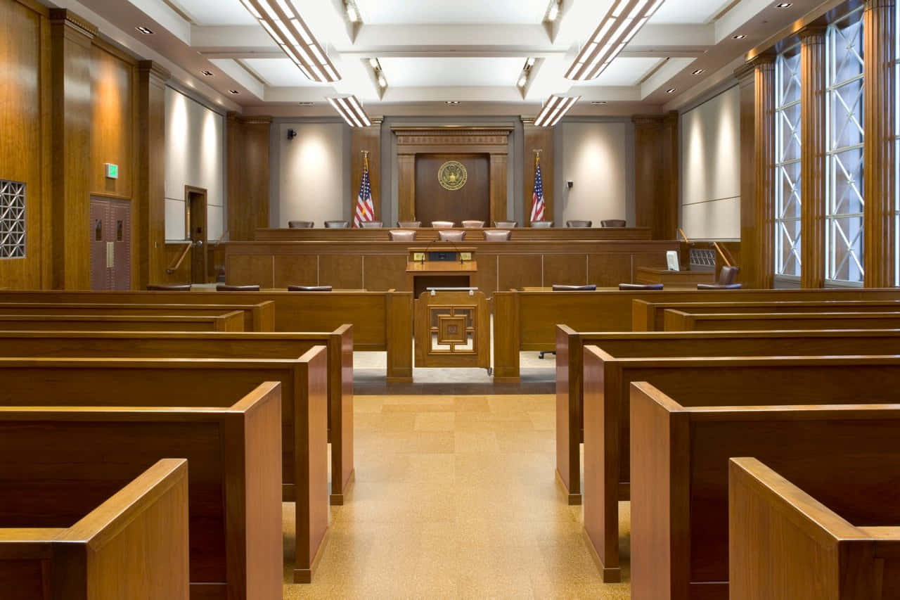 Court 桌布 壁紙 — 一個寬敞空蕩的法庭，配有拋光木長椅和裝飾著美國國旗的法官席。