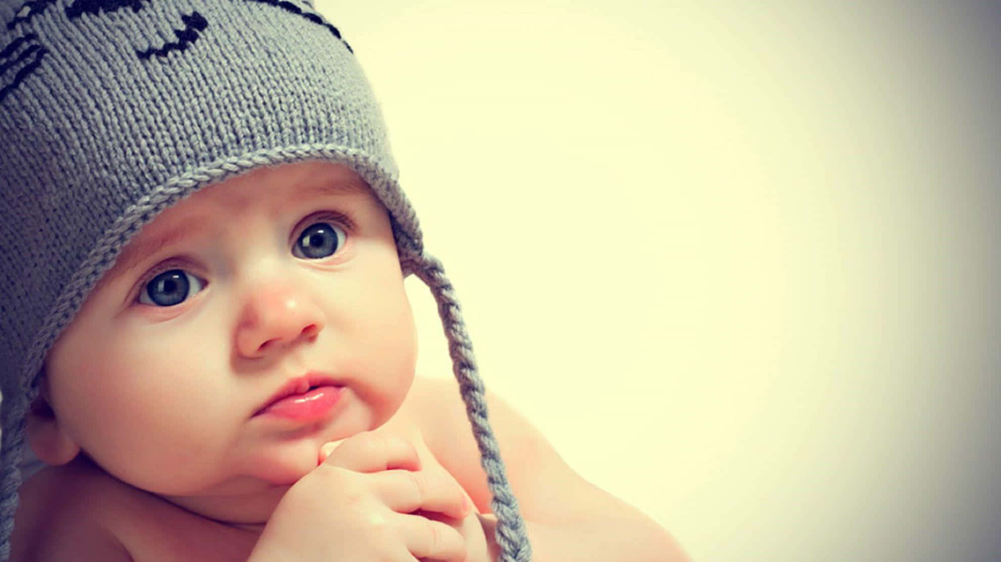 cute baby 桌布 壁紙 — 一個寶寶戴著灰色針織貓臉帽，若有所思地看著鏡頭的特寫。