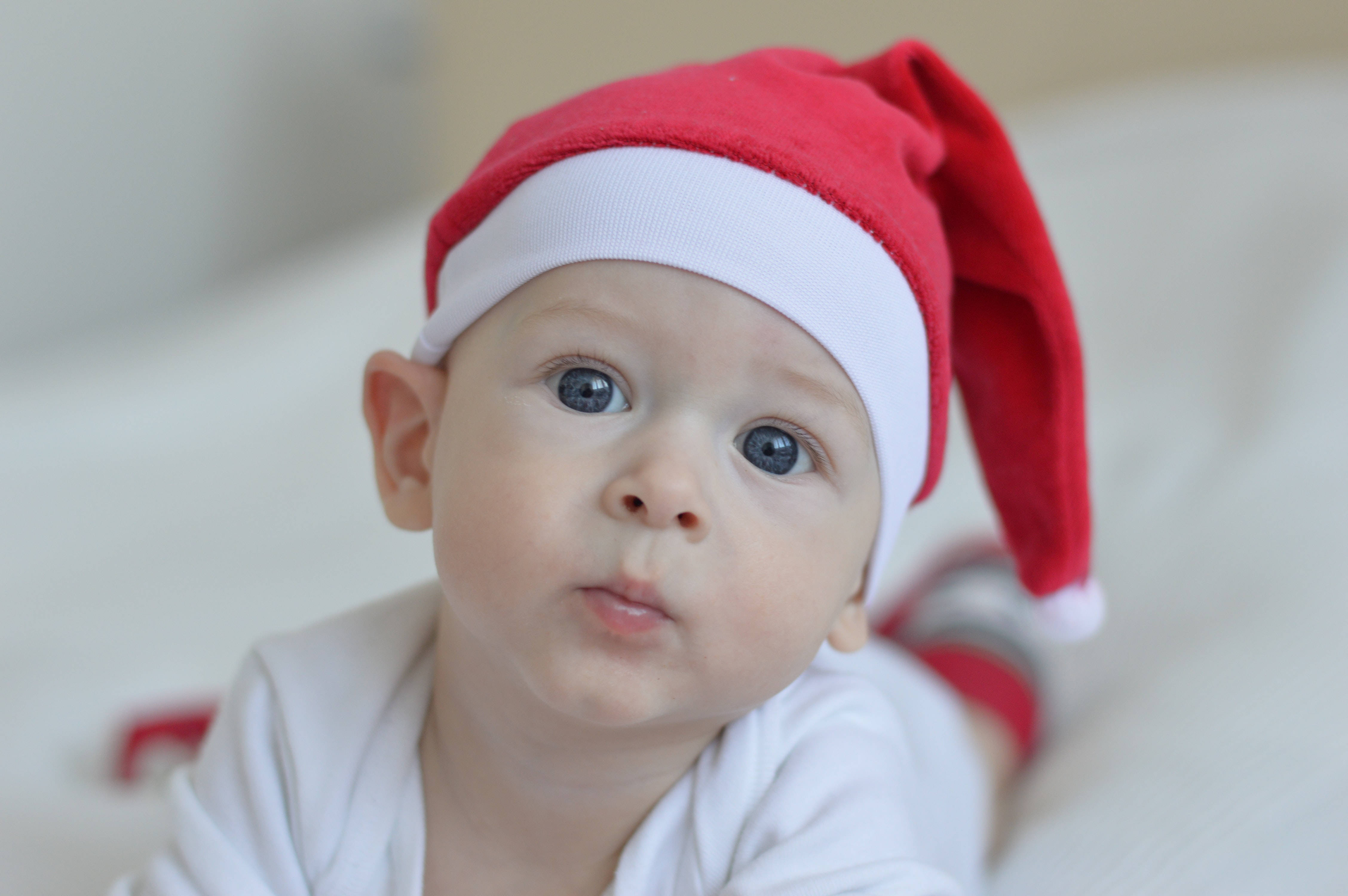 Santa Claus 桌布 壁紙 — 一個寶寶的特寫，戴著紅白聖誕帽，明亮的藍色眼睛好奇地看著鏡頭。