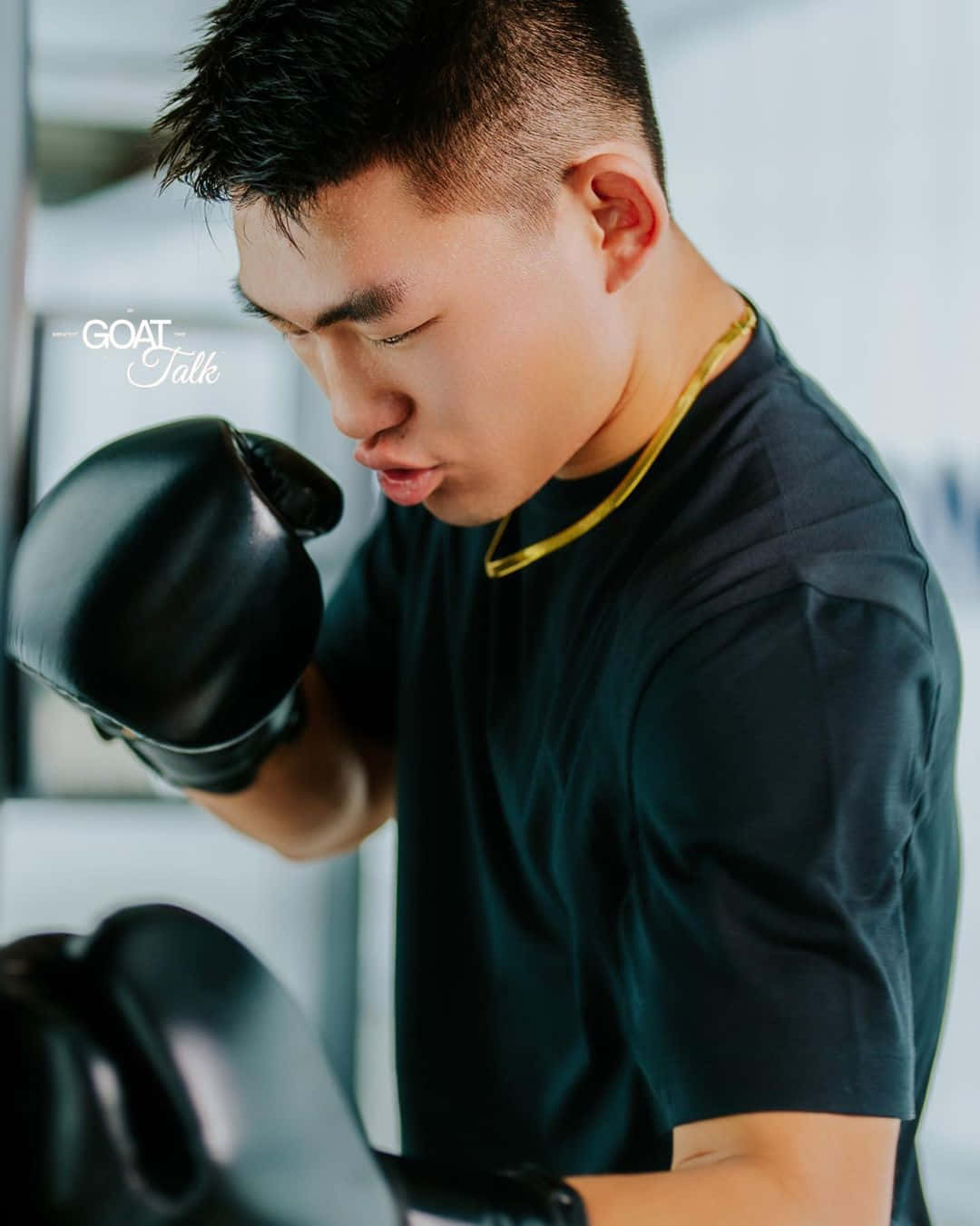 pouty face 桌布 壁紙 — 一個專注的年輕男子戴著黑色拳擊手套，在明亮的健身房裡戴著金鍊項鍊進行激烈訓練。