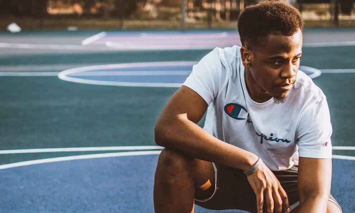 Champion Logo 桌布 壁紙 — 一個專注的年輕男子穿著白色Champion T恤，在黃金時段蹲在充滿活力的藍色戶外籃球場上。