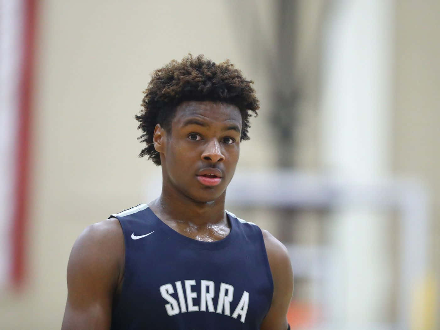 Bronny James 桌布 壁紙 — 一個專注的年輕籃球運動員身穿海軍藍Sierra球衣站在球場上，汗水在皮膚上閃閃發光。