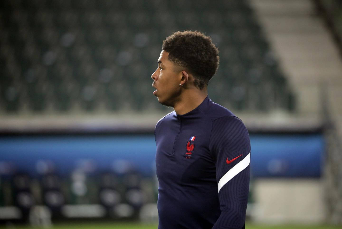 Football Players 桌布 壁紙 — 一個專注的年輕足球員身穿海軍藍法國訓練球衣，獨自站在球場上，在人工燈光下。