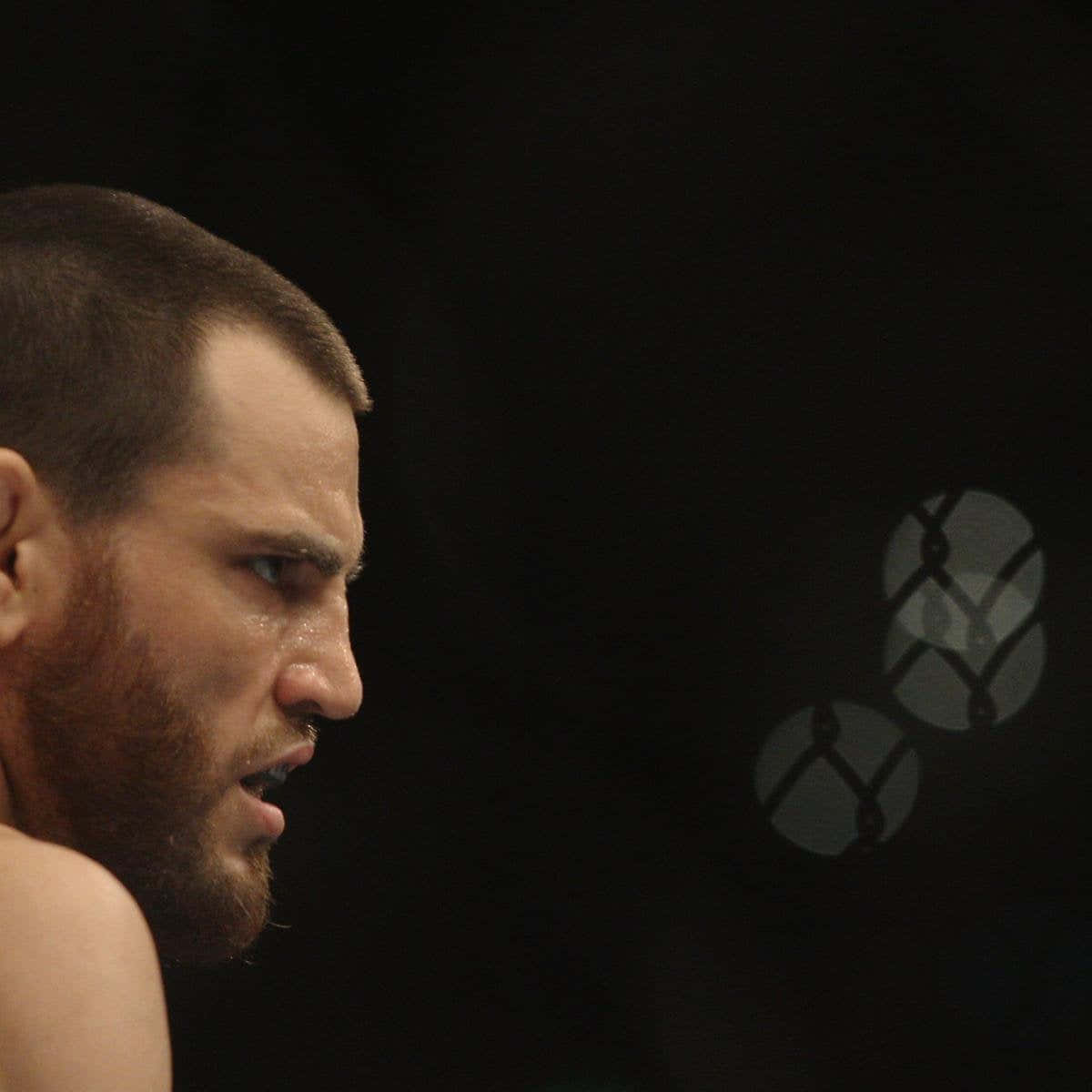 UFC 桌布 壁紙 — 一個專注的拳手，臉上帶著汗水，在昏暗的MMA籠中凝視著。