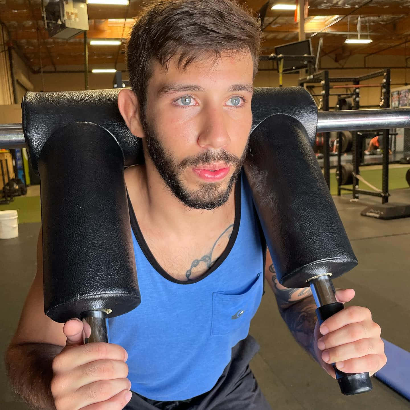 Exercise 桌布 壁紙 — 一個專注的男人，藍眼睛和刺青，在光線充足的健身房裡抓住一台黑色的重量訓練機。