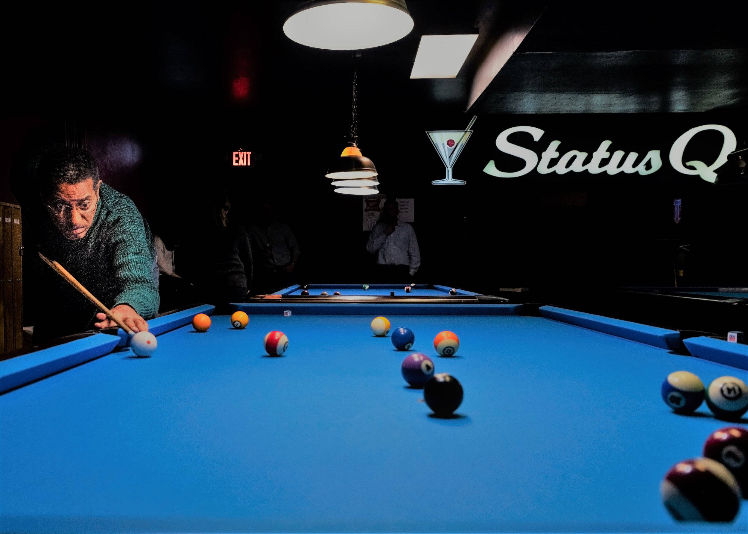 Pool Table 桌布 壁紙 — 一個專注的男人俯身在一張充滿活力的藍色撞球桌上，身處燈光昏暗的酒吧，背後有發光的「Status Q」標誌。