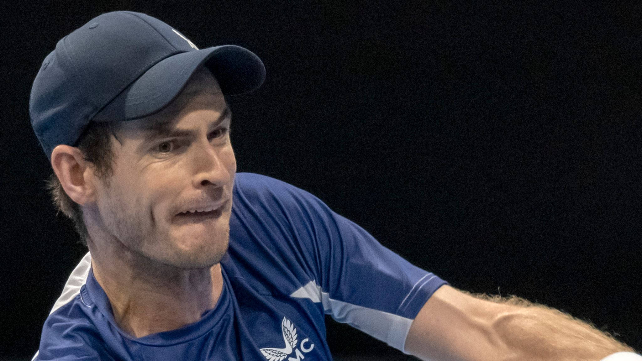 Tennis 桌布 壁紙 — 一個專注的男性網球運動員，戴著藍色帽子和穿著藍色襯衫，在深色背景下揮拍。