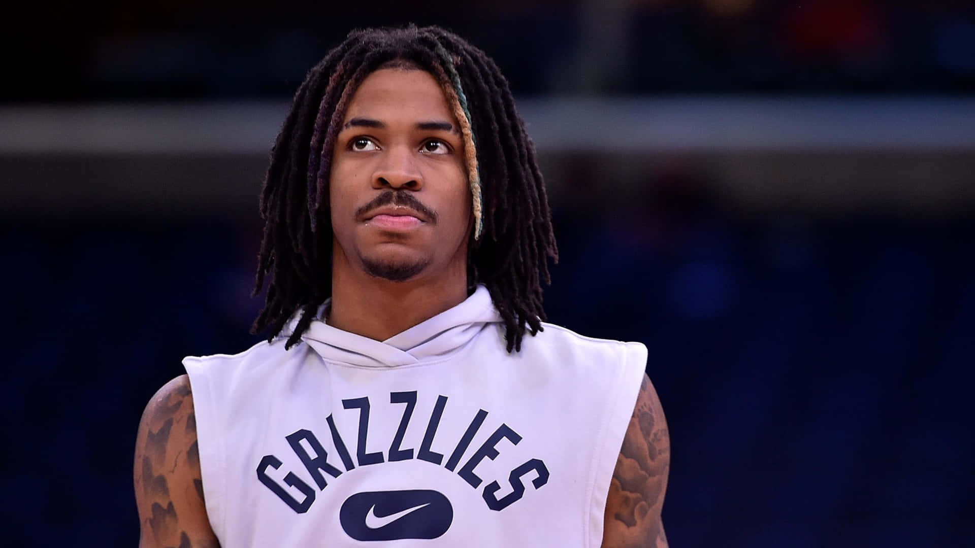 Ja Morant 動圖 桌布 壁紙 — 一個專注的籃球運動員，梳著辮子頭和紋身，穿著白色灰熊隊無袖連帽衫，背景是黑暗的球場。