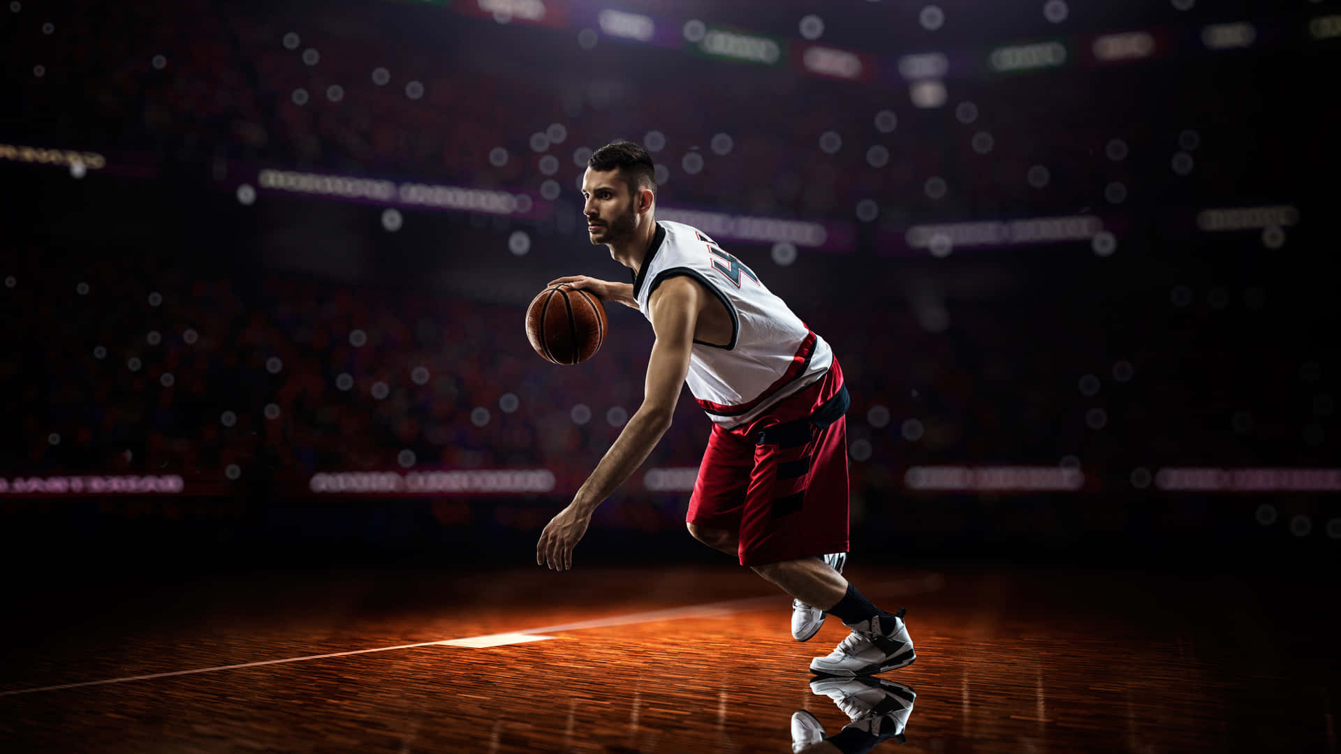 1080p Basketball 桌布 壁紙 — 一個專注的籃球運動員在場館燈光下激烈運球，背景是模糊的人群。