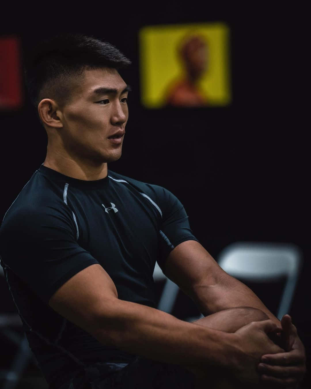 Exercise 桌布 壁紙 — 一個專注的肌肉男穿著黑色運動衫坐在光線昏暗的健身房裡，身後有一張模糊的黃色海報。