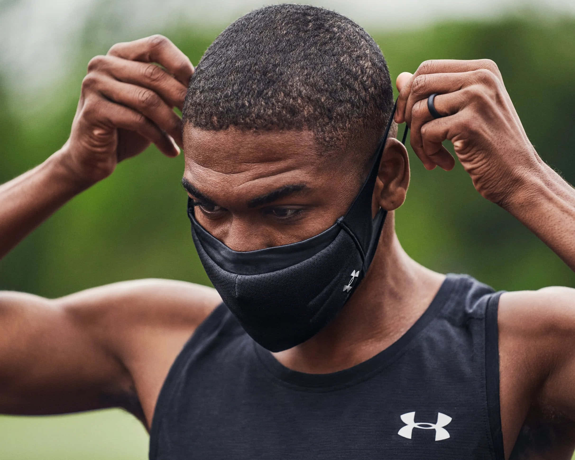 Under Armour 桌布 壁紙 — 一個專注的運動型男士在戶外穿著品牌背心時調整黑色口罩。