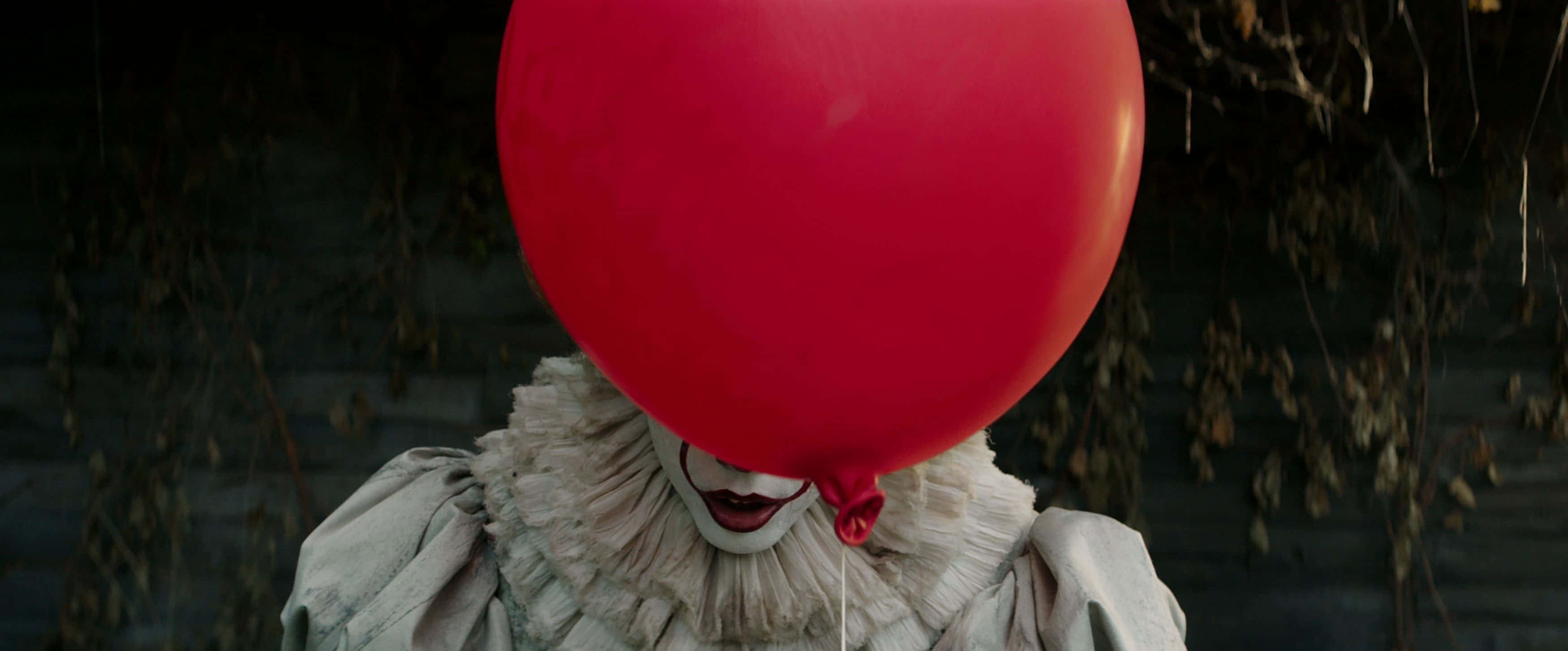 It 2017 桌布 壁紙 — 一個小丑用紅色氣球遮住臉，站在黑暗無葉的背景前。