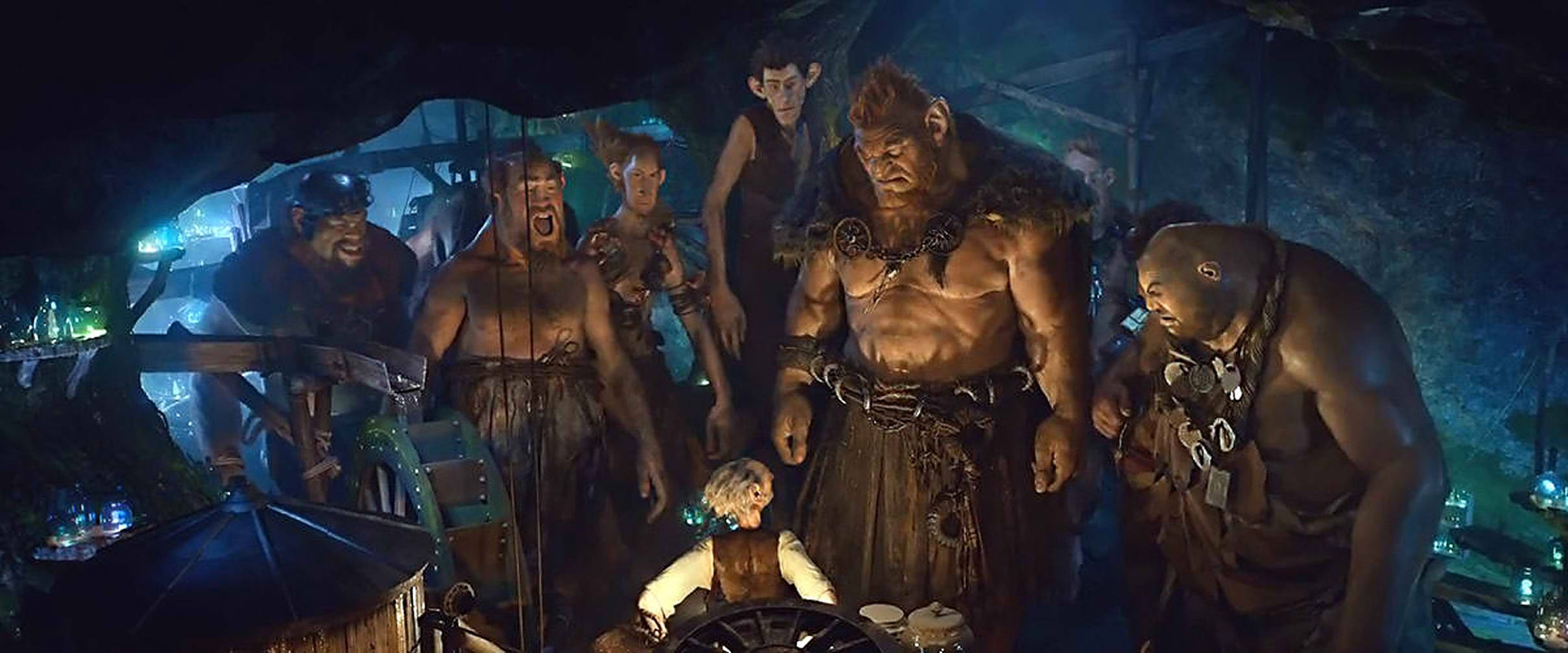 Bfg 桌布 壁紙 — 一個小人坐在輪子旁，被高聳憤怒的食人魔包圍，在一個昏暗的洞穴中，有發光的藍色燈光。