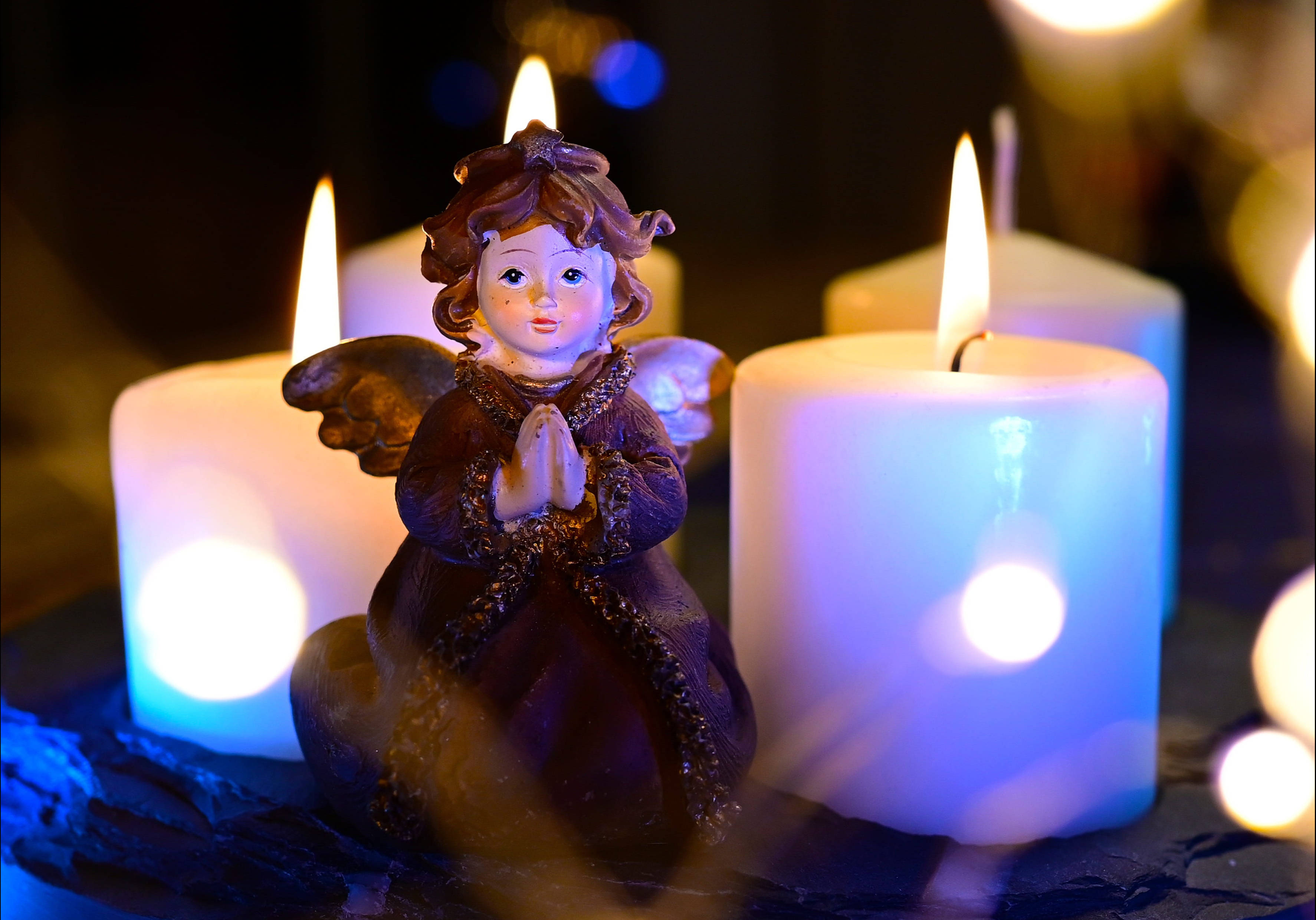 angels 桌布 壁紙 — 一個小型天使雕像跪著祈禱，被發光的白色蠟燭包圍，在黑暗環境中投射出柔和的藍光。