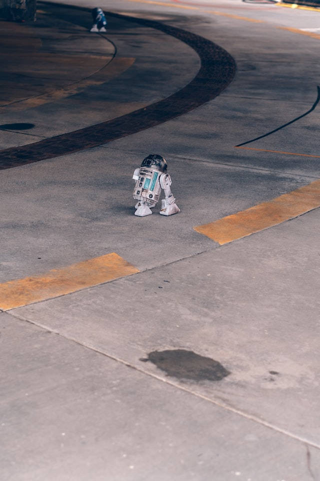 星際大戰 iPhone 桌布 壁紙 — 一個小型機器人獨自站在一條彎曲的混凝土路上，路上有褪色的黃線，在柔和日光下。