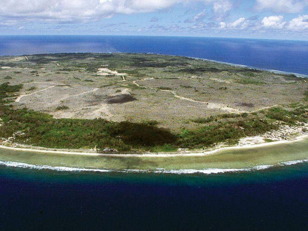 島嶼 桌布 壁紙 — 一個小型熱帶島嶼的鳥瞰圖，擁有沙灘、珊瑚礁和稀疏植被，被深藍色海洋環繞。