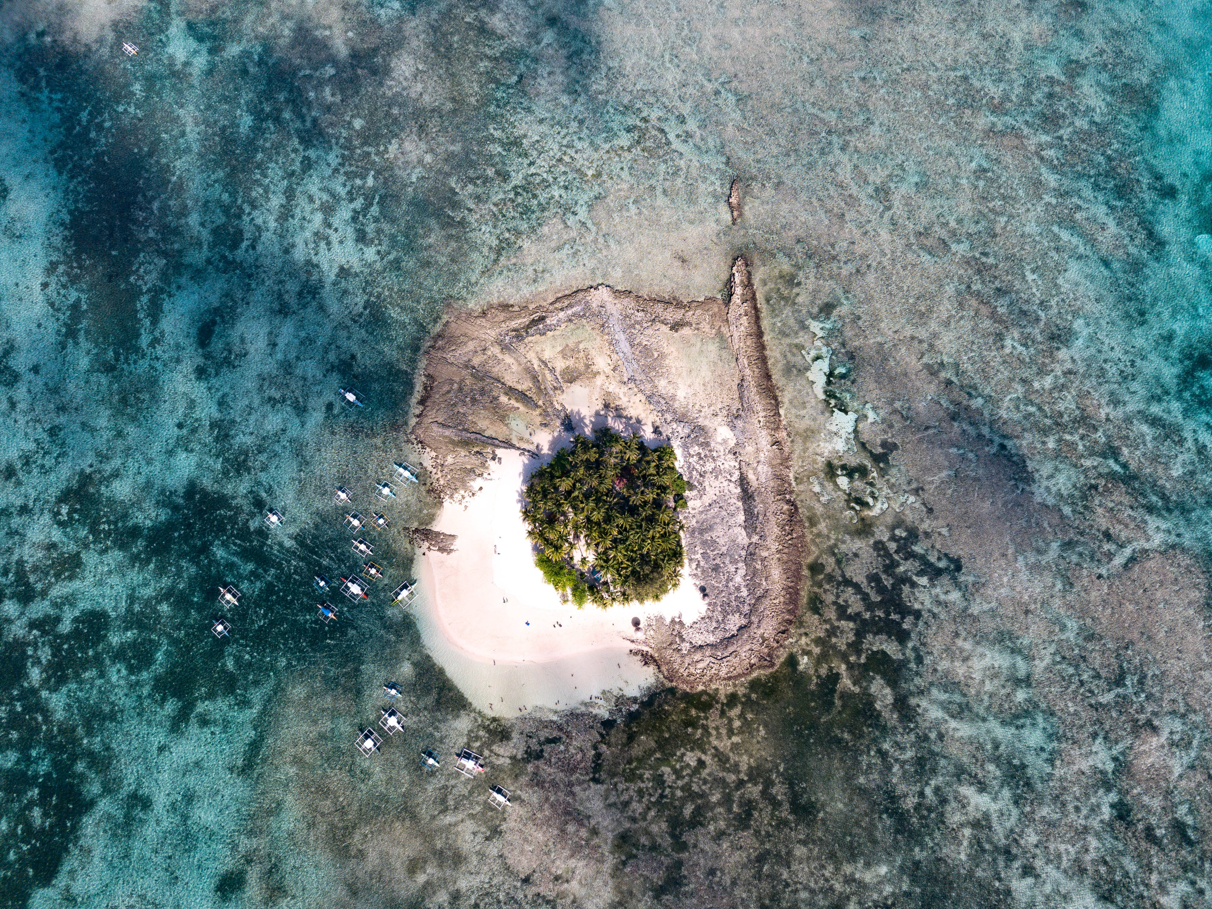 Siargao 桌布 壁紙 — 一個小型熱帶島嶼的鳥瞰圖，擁有白色沙灘和茂密的綠色樹木，周圍是碧綠的海水，附近停泊著船隻。