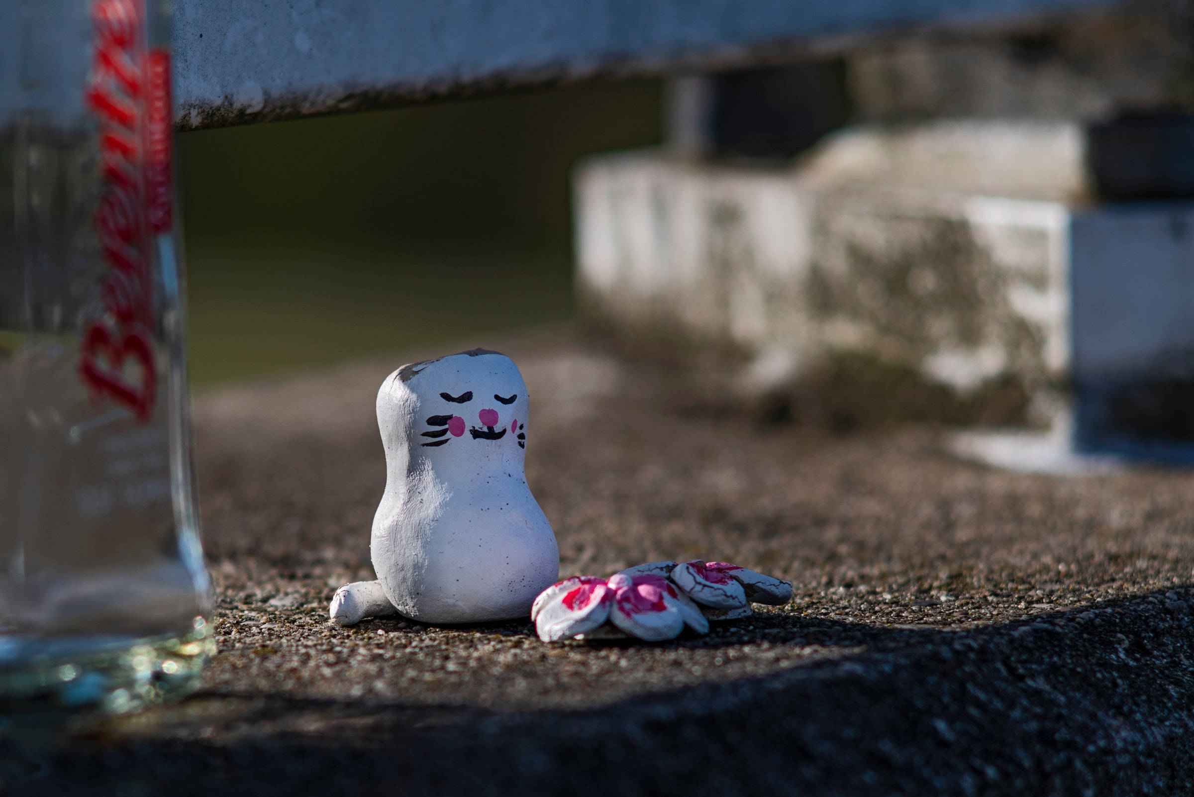 Remembrance 桌布 壁紙 — 一個小型白色塗漆貓公仔，臉頰粉紅，坐在長凳下，旁邊散落著糖果，午後柔和光線中。