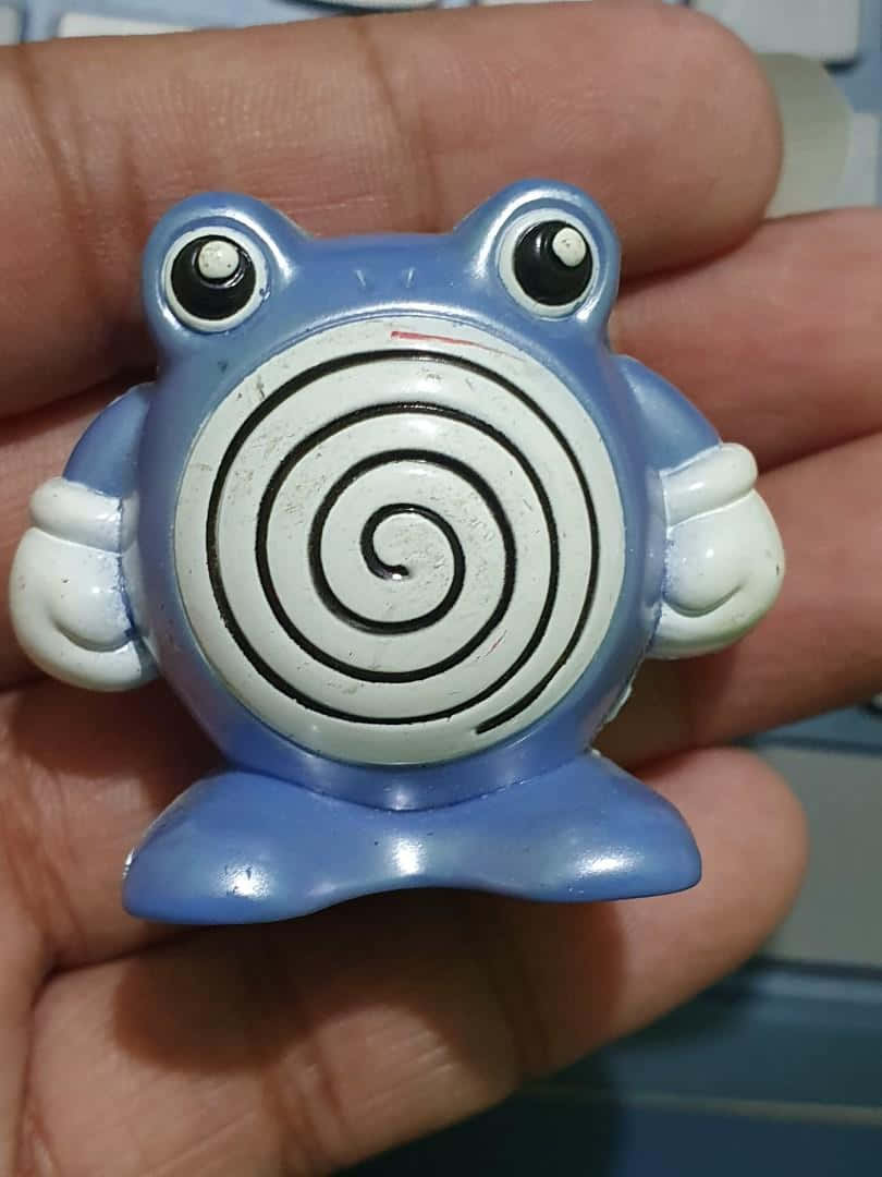 Pokemon Aesthetic 桌布 壁紙 — 一個小型的藍色塑膠青蛙公仔，腹部有螺旋圖案，被握在一個人的手中。