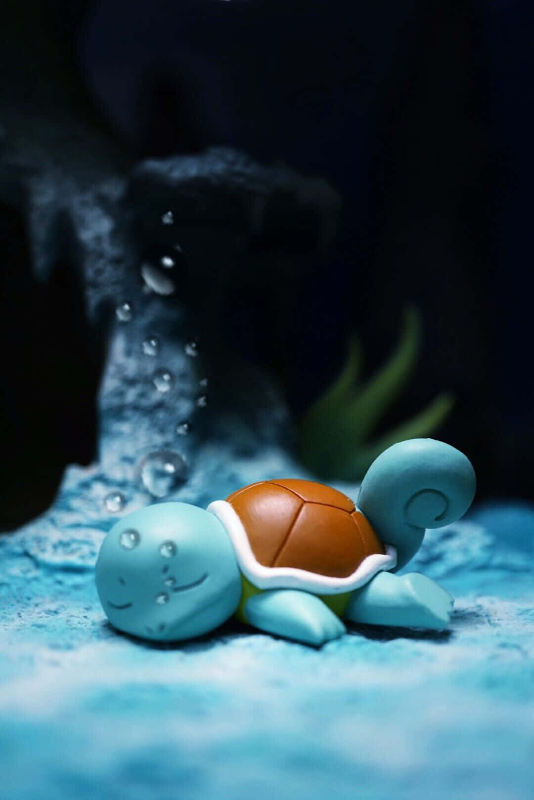 Pokemon Figures 桌布 壁紙 — 一個小型的藍色海龜雕像放置在帶有紋理的藍色表面上，背後有氣泡在黑暗的水下場景中升起。