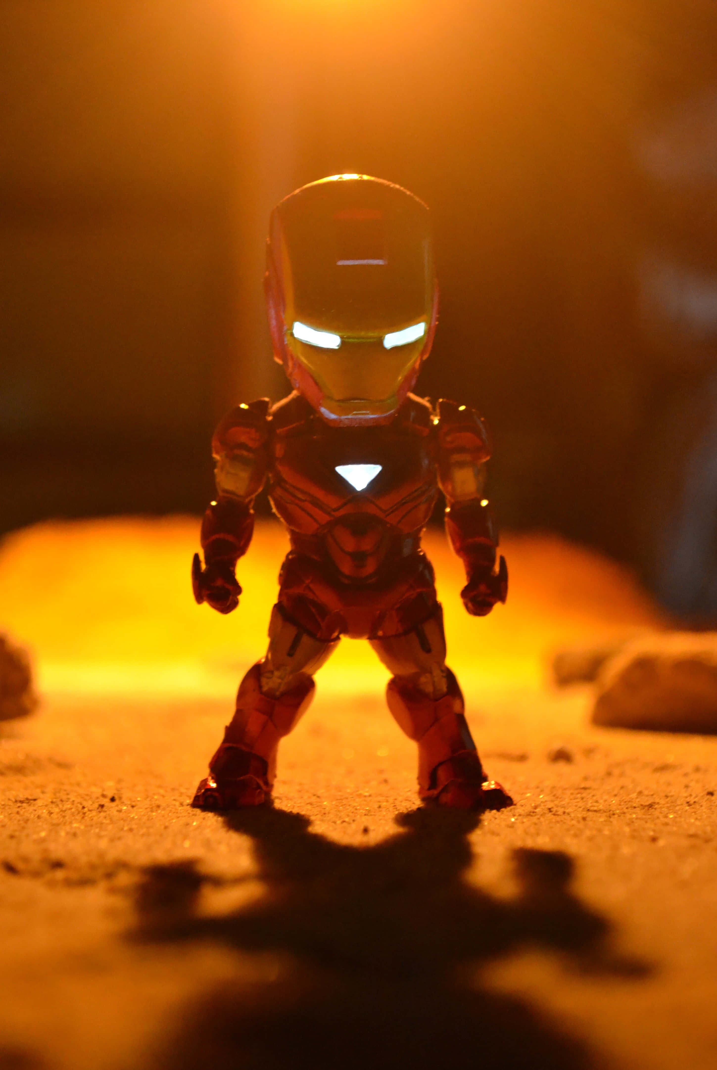 Iron Man Action Figures 桌布 壁紙 — 一個小型的鋼鐵人動作人偶在溫暖的金色光線照射下，在紋理地面上投下清晰的陰影。