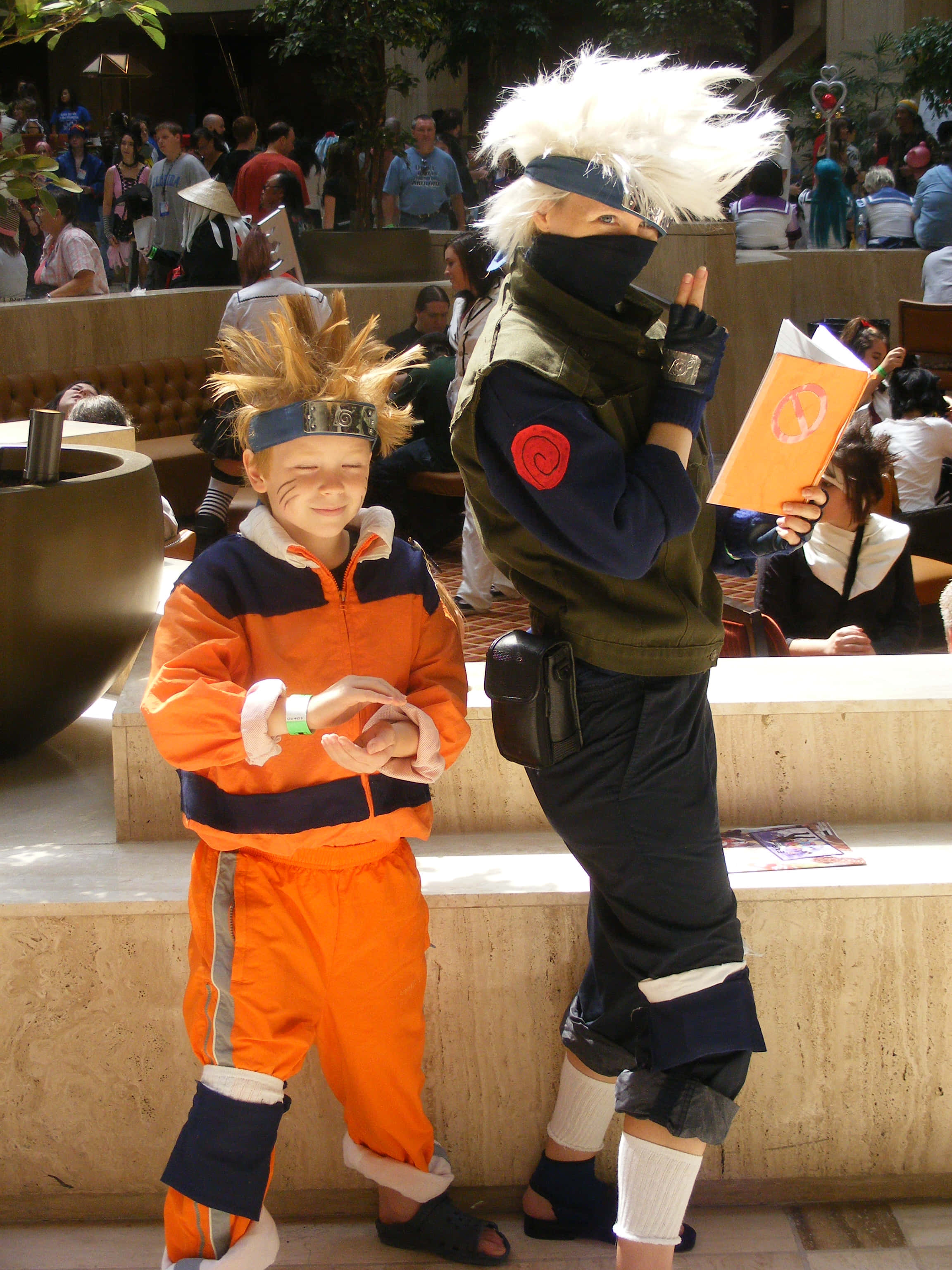 Kakashi And Naruto 桌布 壁紙 — 一個小孩和一個大人穿著鮮豔的火影忍者cosplay，在擁擠的戶外展會上開心地擺姿勢。