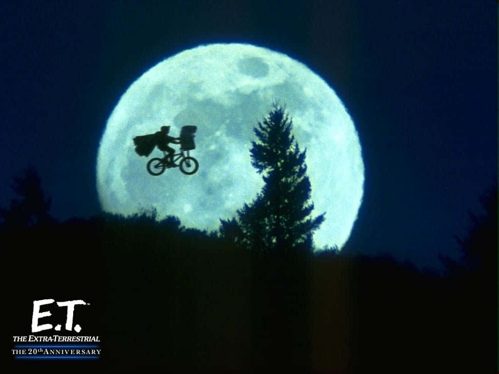 Et 桌布 壁紙 — 一個小孩和外星人騎著腳踏車，對著黑暗森林輪廓上方一個巨大的發光月亮。