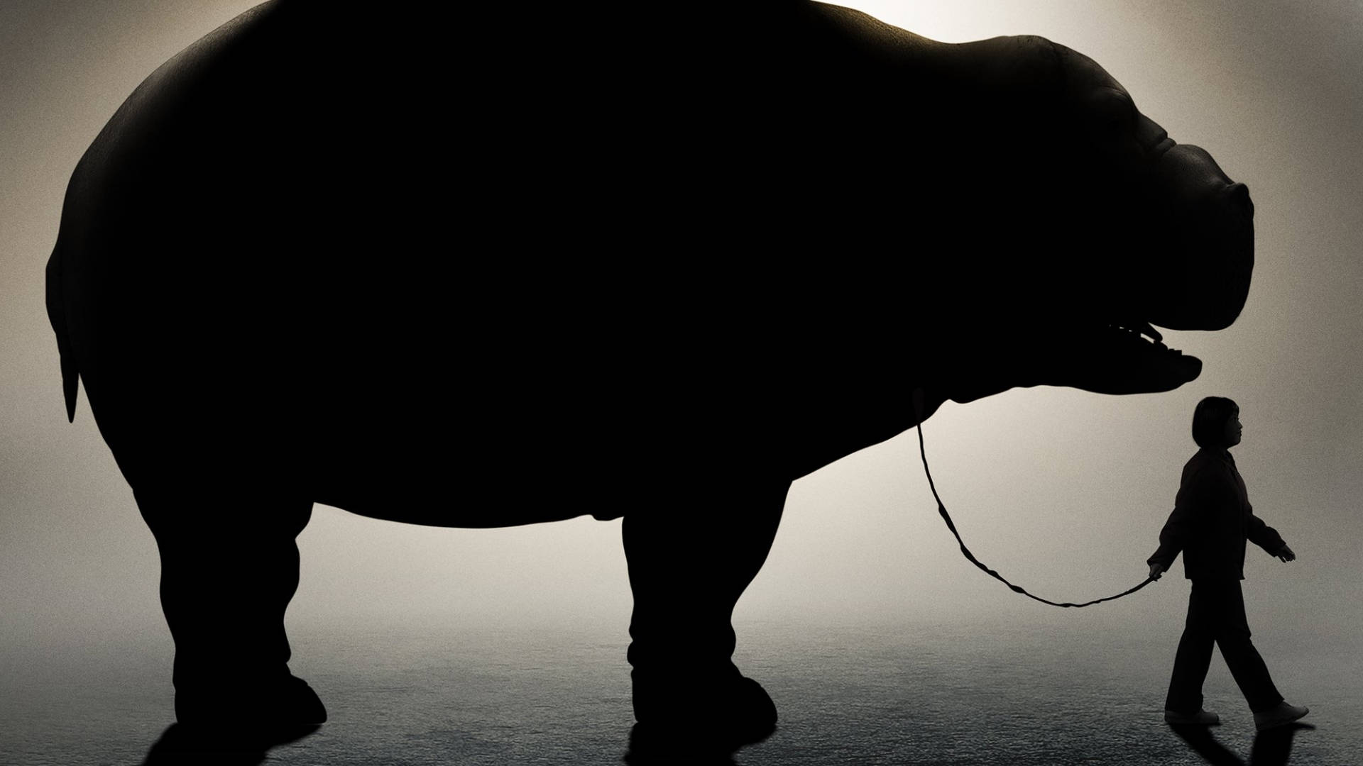 okja 桌布 壁紙 — 一個小孩在霧氣瀰漫的工作室裡用皮帶牽著一隻巨大的河馬散步，背景光線戲劇性。