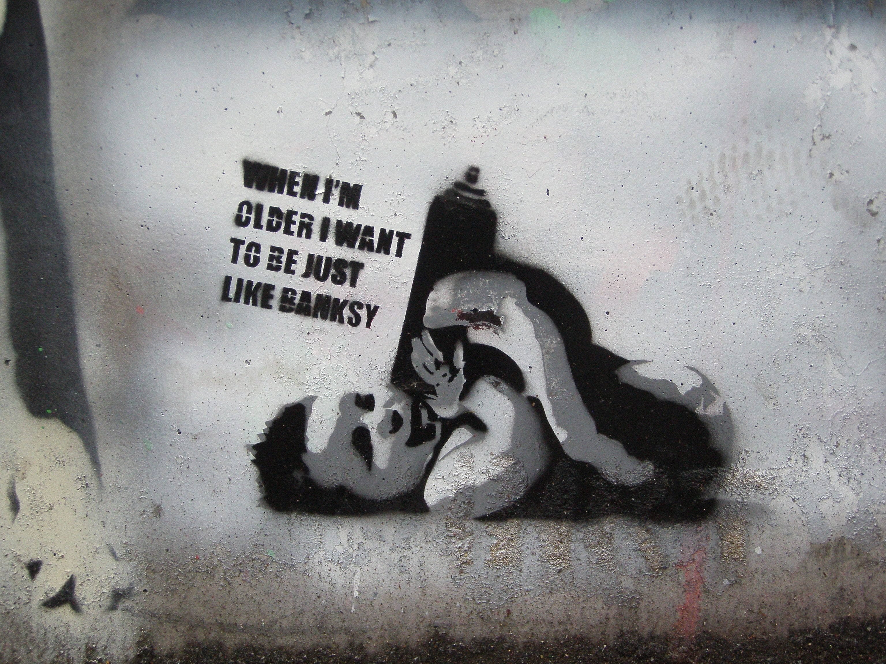 Banksy 桌布 壁紙 — 一個小孩拿著噴漆罐的模板塗鴉藝術作品，上面寫著「當我長大後，我想像Banksy一樣」在風化的牆上。