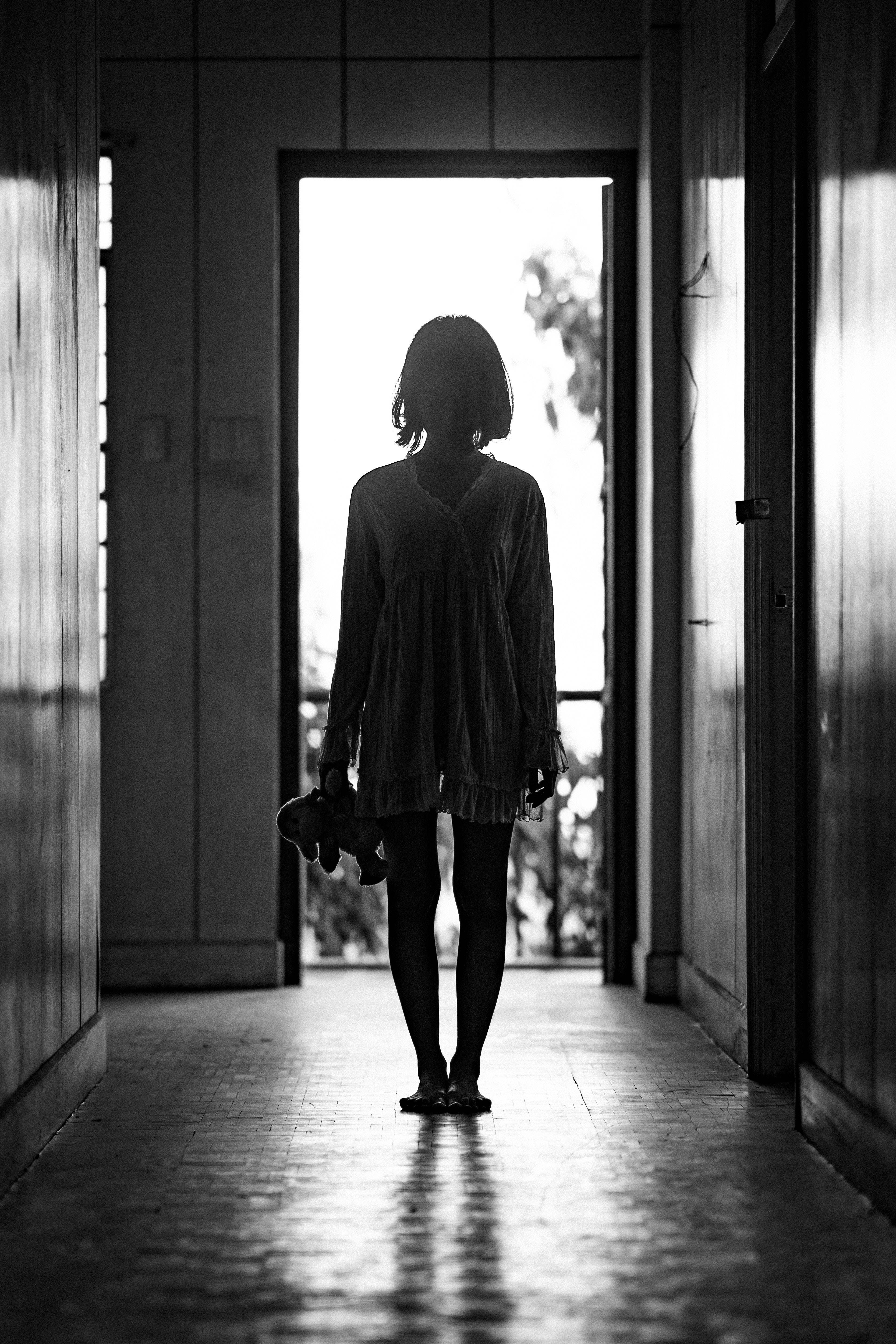 詭異的GIF 桌布 壁紙 — 一個小孩的剪影站在昏暗走廊的盡頭，抱著絨毛玩具，背光來自明亮的室外光線。