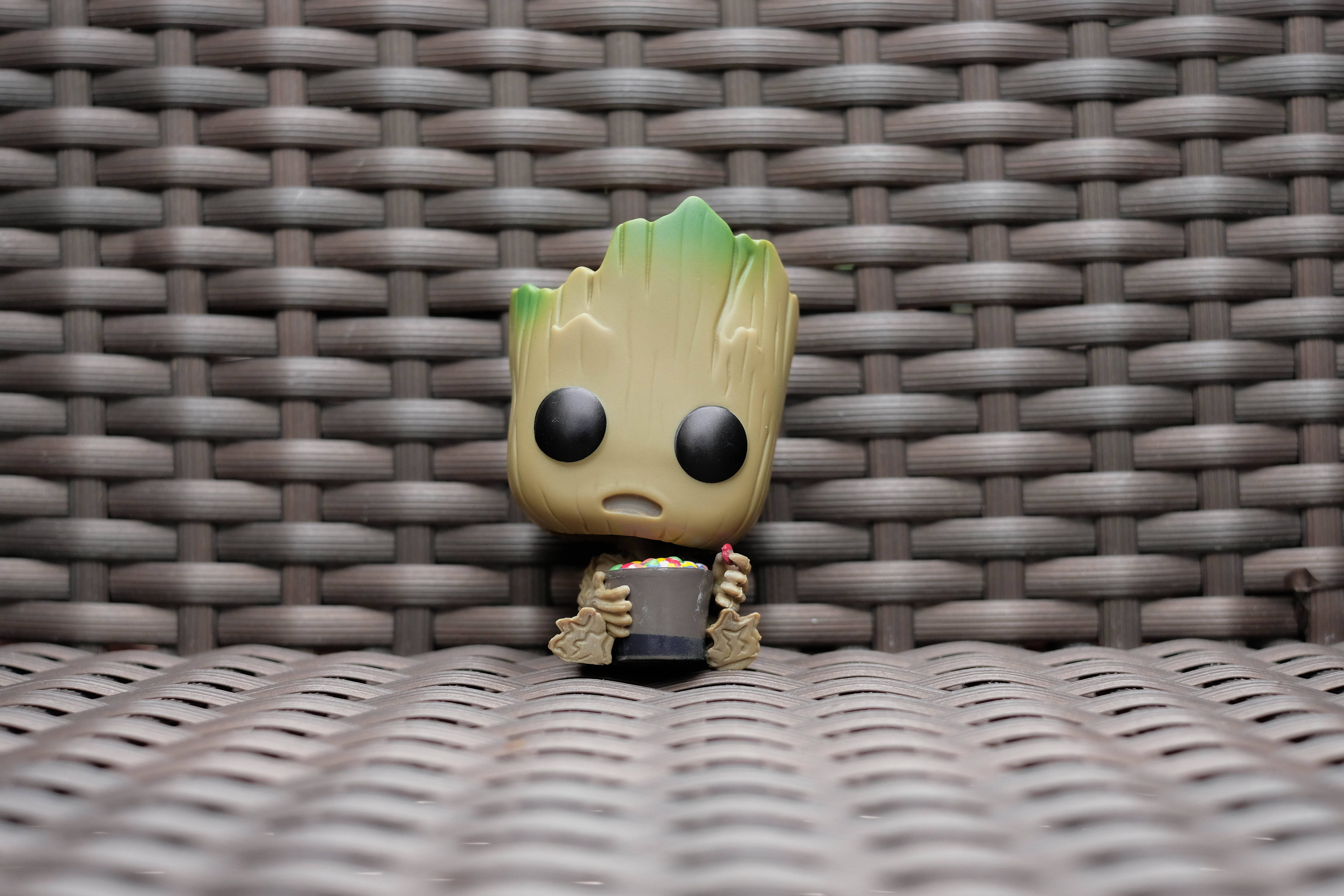 格魯特 桌布 壁紙 — 一個小小的Groot Funko Pop公仔坐在一張編織的棕色戶外椅子上，拿著一杯色彩繽紛的糖果。