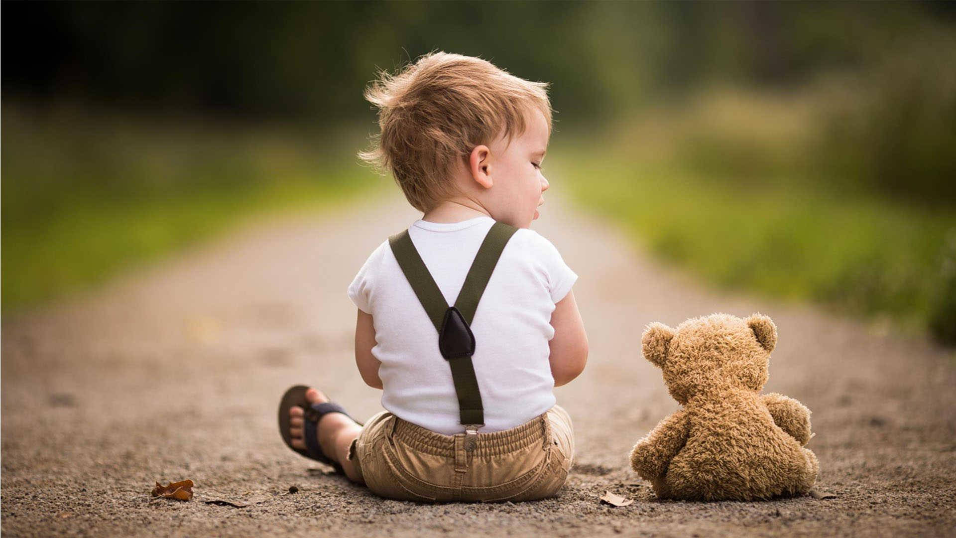 Teddy Bear 桌布 壁紙 — 一個小朋友坐在泥路上，旁邊有一隻泰迪熊，凝視遠方，環境寧靜。