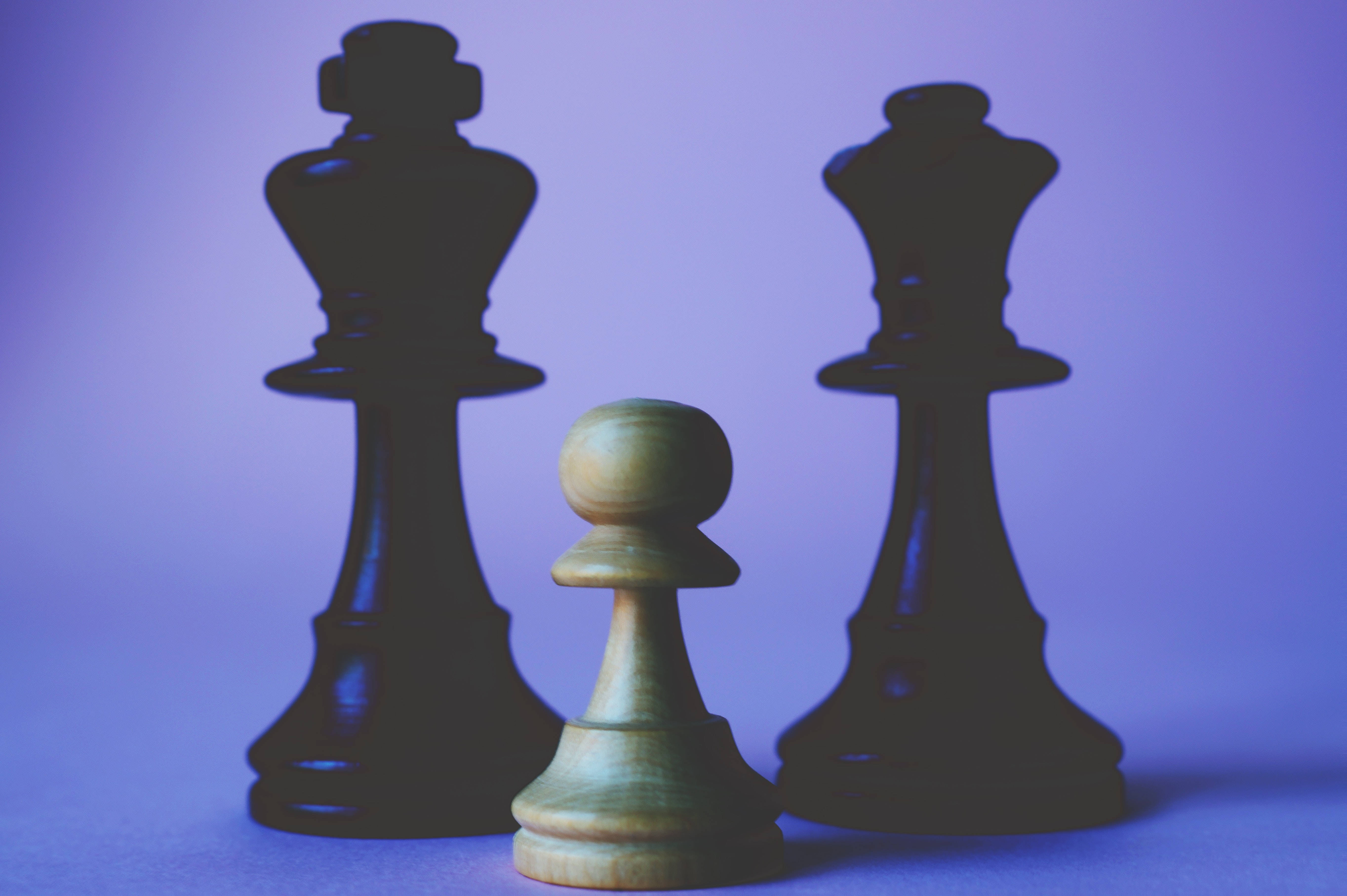 黑色與紫色 桌布 壁紙 — 一個小木兵站在兩個高聳的黑色國王棋子之間，背景是柔和的紫色漸層。