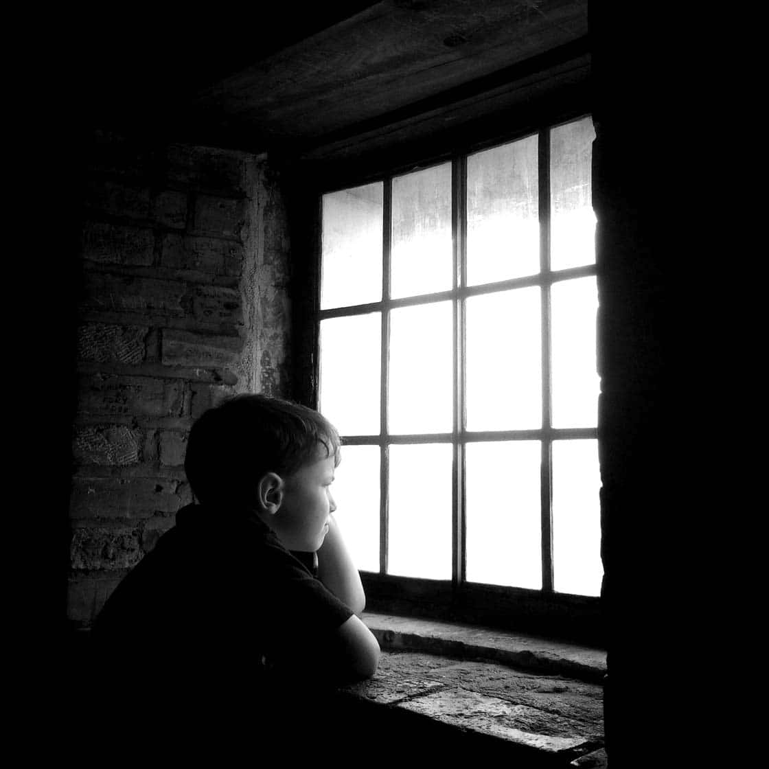 Aesthetic Black And White 桌布 壁紙 — 一個小男孩以剪影形式坐在石窗台上，透過明亮的鑲板窗戶望向光線昏暗的磚房外。