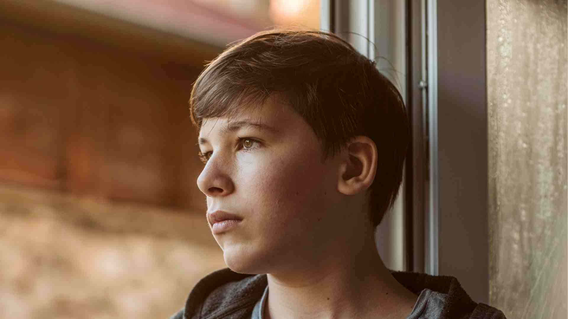 Hot Teen Boy 桌布 壁紙 — 一個小男孩沉思地望著窗外，溫暖的金色陽光灑在他身上，突顯了他沉思的表情。