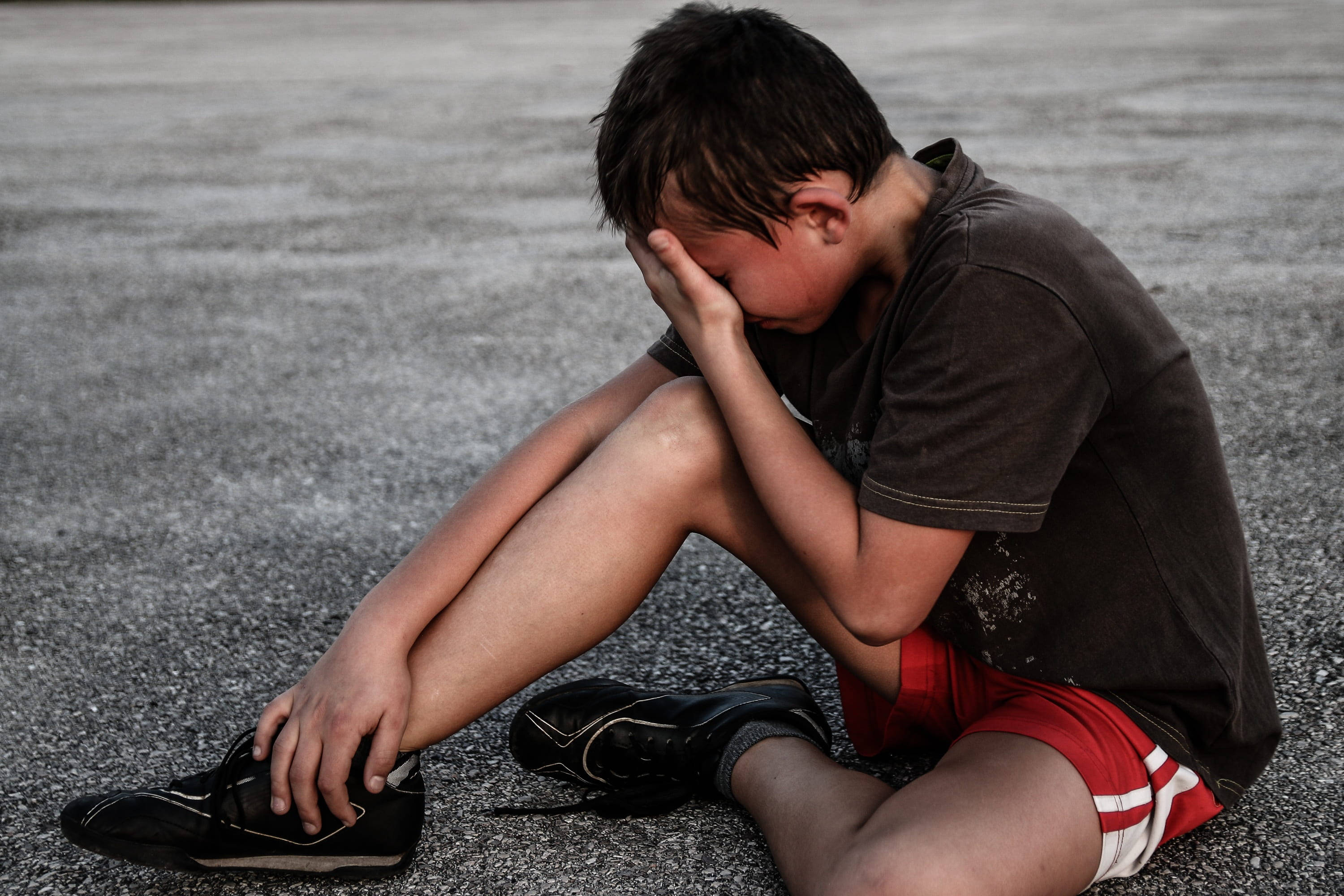 crying sad boy 桌布 壁紙 — 一個小男孩獨自坐在柏油路上，雙手抱頭，傳達出深深的悲傷和孤獨。