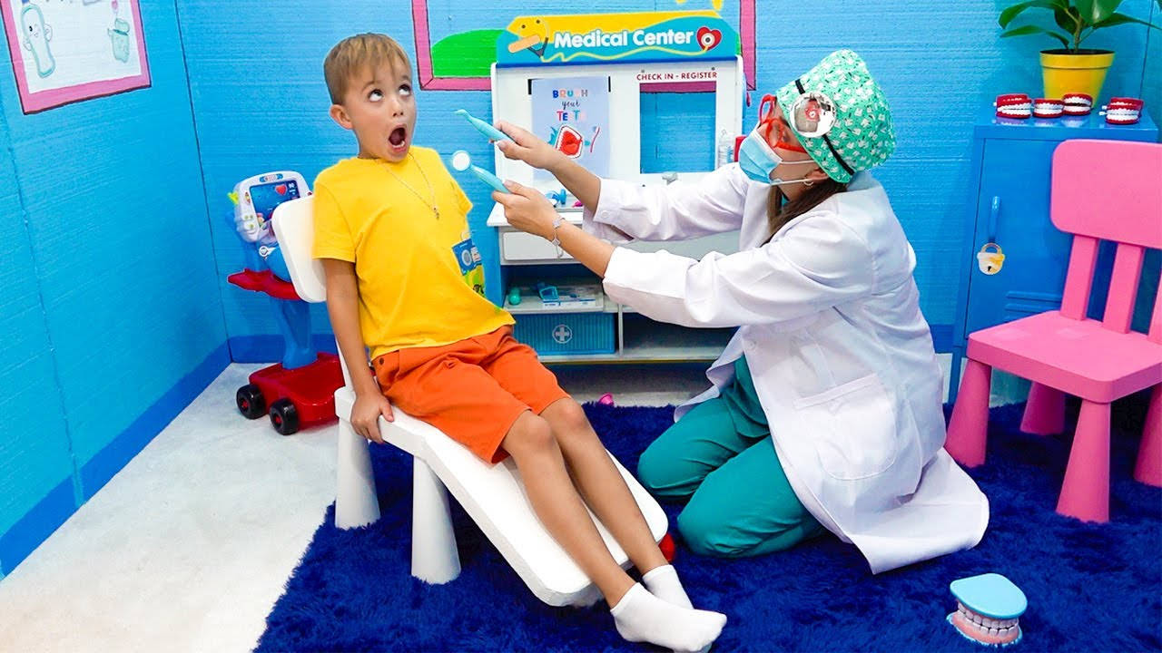 Dentistry 桌布 壁紙 — 一個小男孩睜大眼睛坐在玩具牙科椅上，在色彩繽紛的診所裡，一位頑皮的牙醫用玩具鏡子檢查他的牙齒。