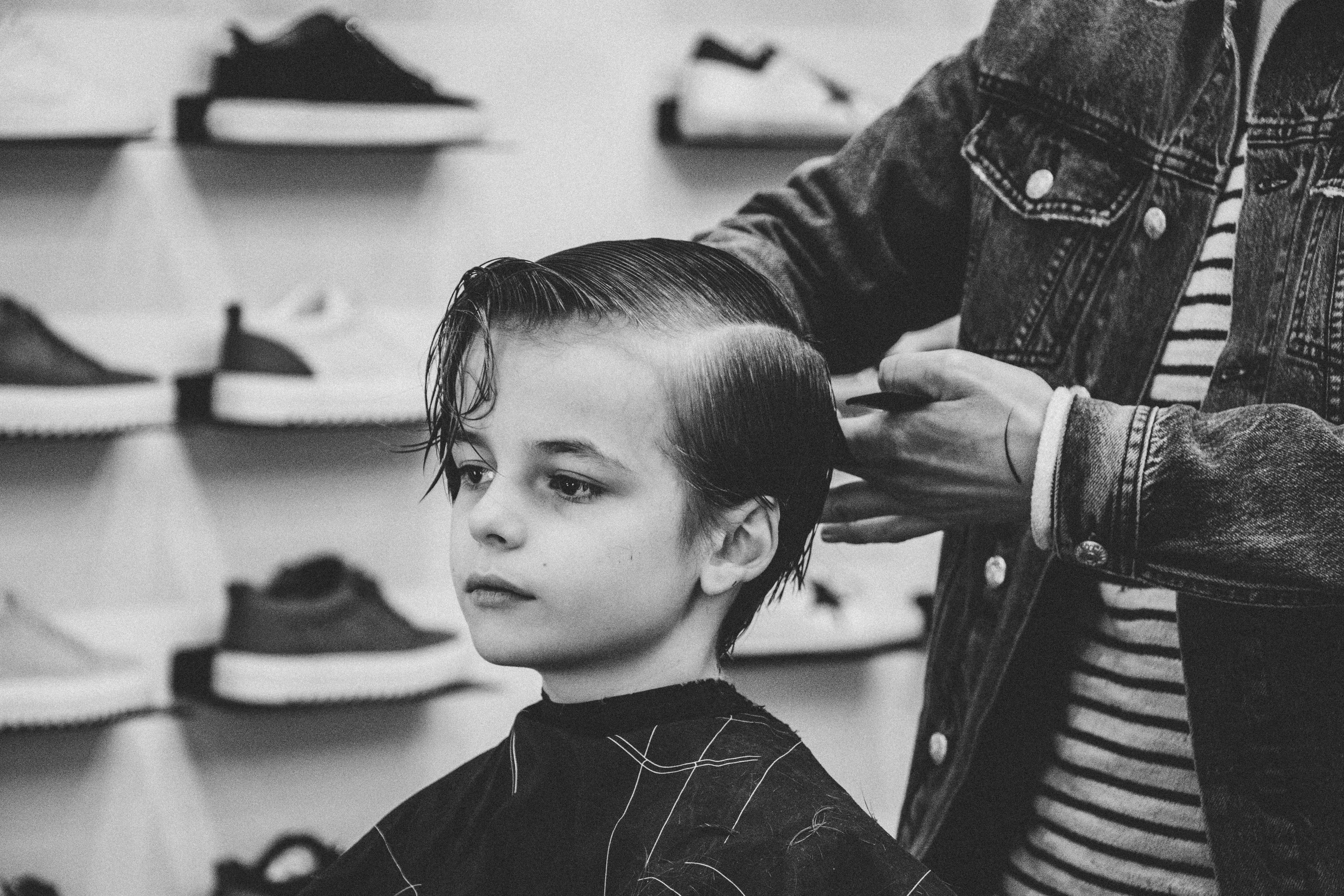 Haircut 桌布 壁紙 — 一個小男孩耐心地坐著，造型師在單色調理髮店為他修剪頭髮，身後的架子上陳列著運動鞋。