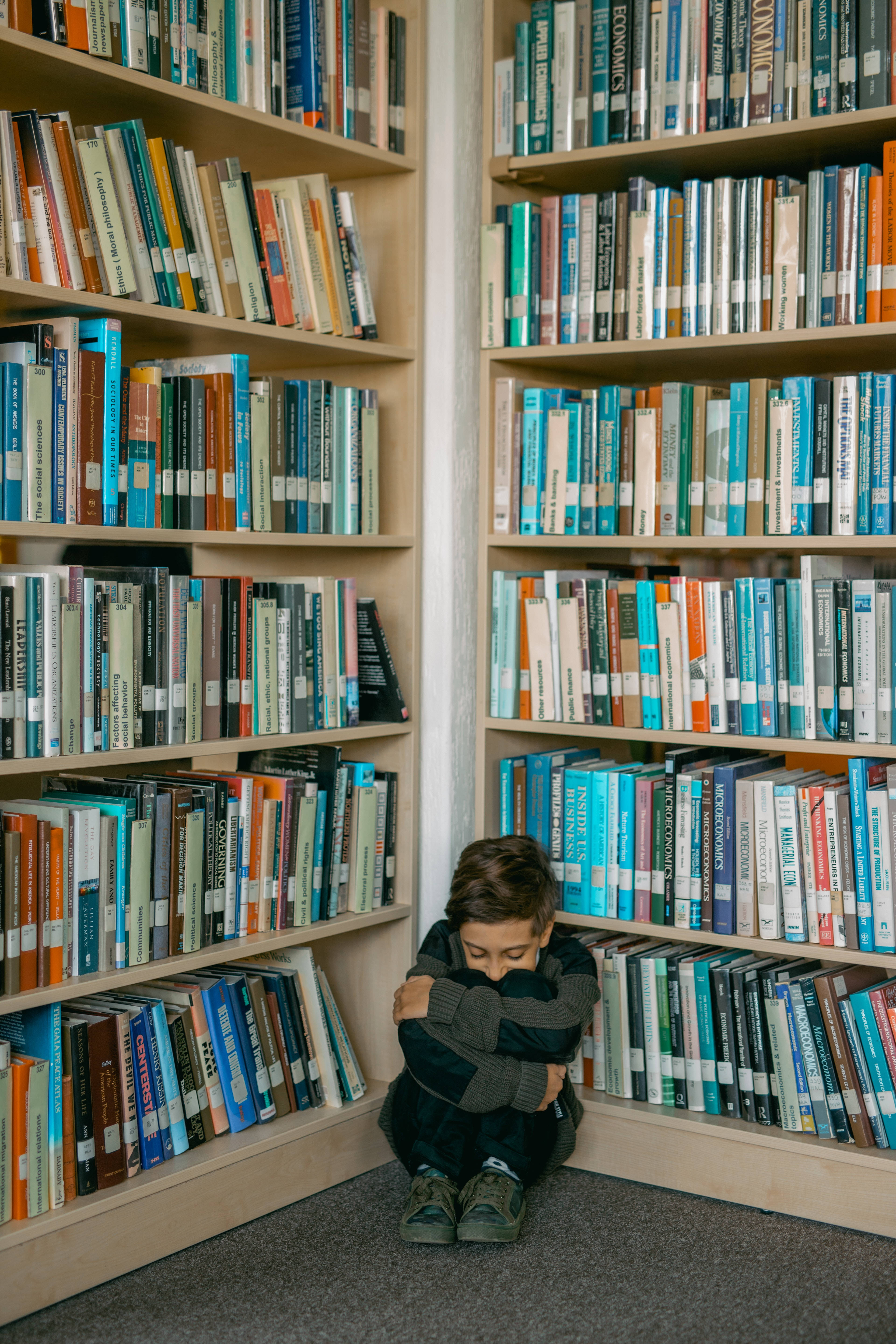 桌布 壁紙 — 一個小男孩蜷縮在圖書館的角落，周圍是高聳的書架，上面擺滿了色彩繽紛的書籍。