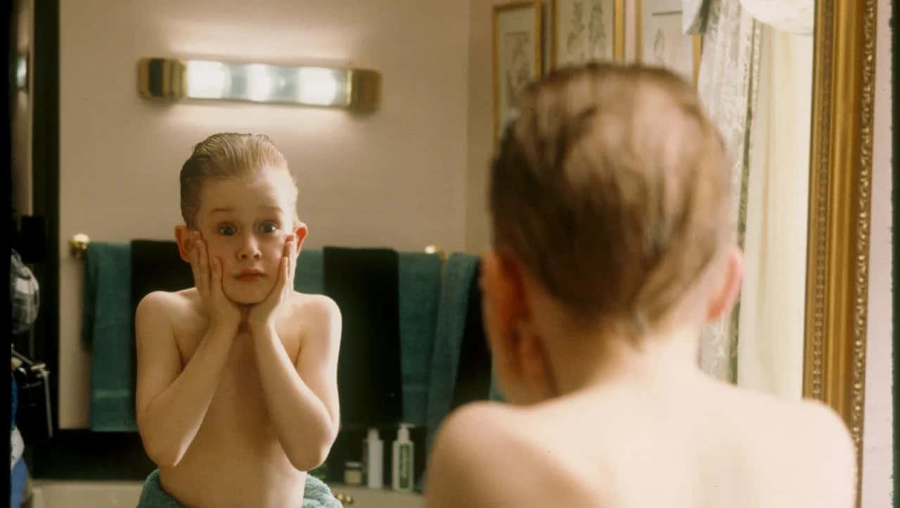 Home Alone 桌布 壁紙 — 一個小男孩雙手托腮，睜大眼睛盯著浴室鏡子中的倒影。
