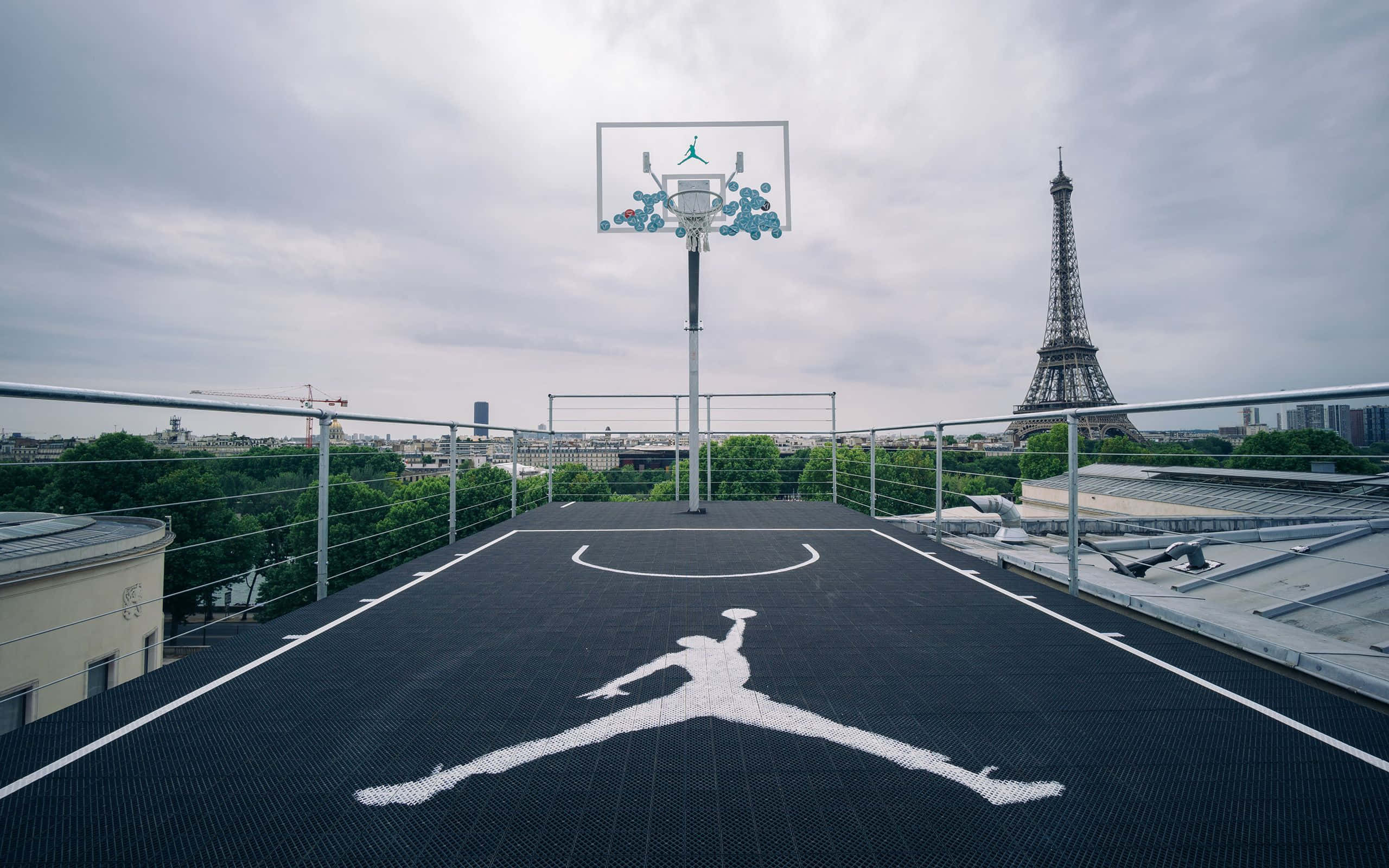 Basketball Court 桌布 壁紙 — 一個屋頂籃球場，帶有巨大的喬丹標誌和籃框，俯瞰巴黎，遠處的艾菲爾鐵塔在陰天之下。
