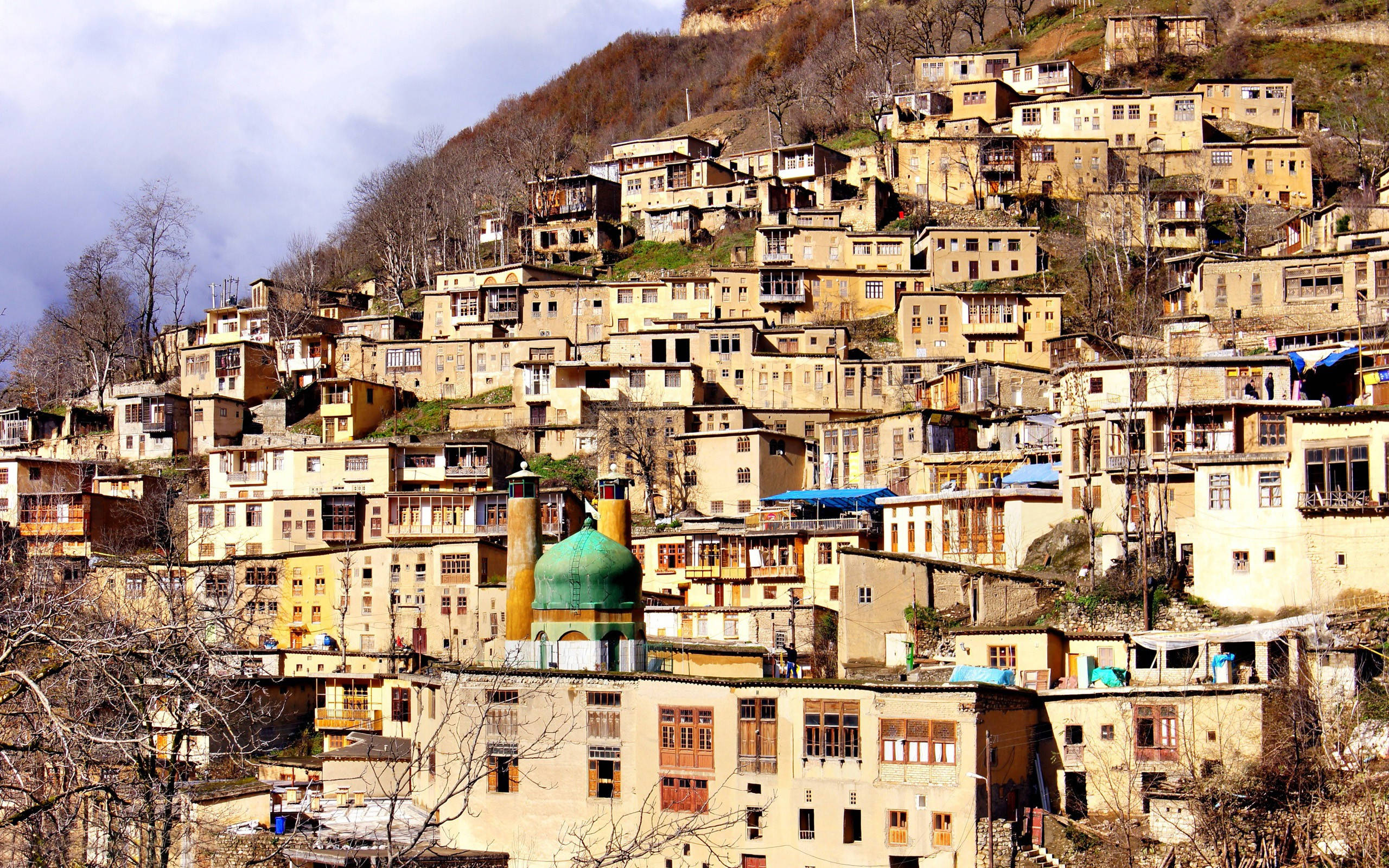 Tehran 桌布 壁紙 — 一個山坡村莊，有梯田式的石屋和一座綠色圓頂清真寺，天空多雲。