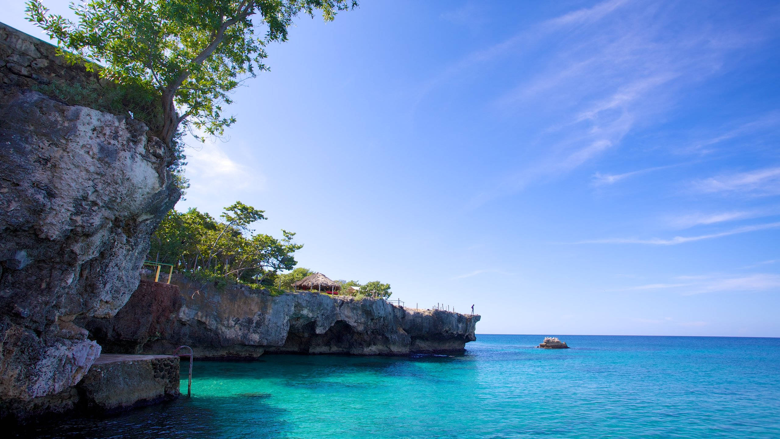 Jamaica 桌布 壁紙 — 一個岩石峭壁，長滿茂密的綠色植物，俯瞰著明亮藍天下清澈的碧綠海水。