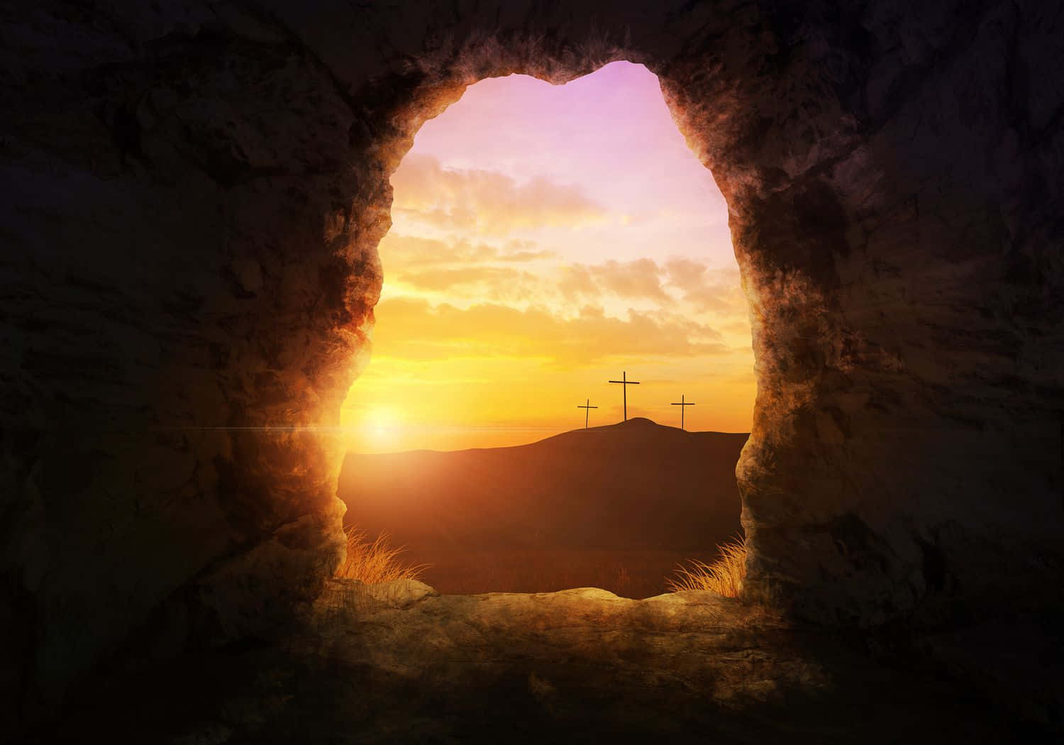 Gospel 桌布 壁紙 — 一個岩石洞穴入口框住了一個日出，山丘上有三個十字架的剪影襯著金色雲層。